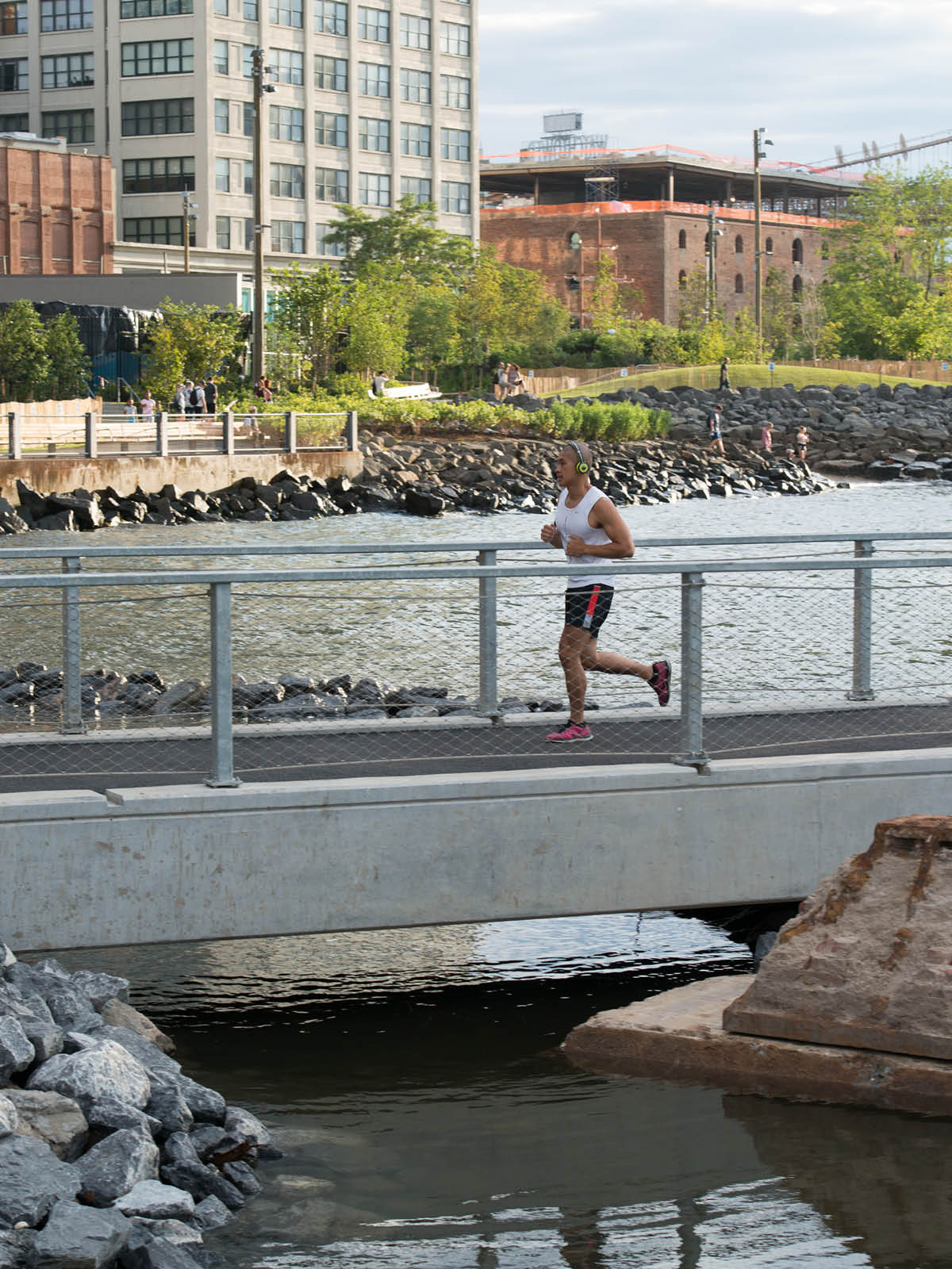 Man running on pedestrian walkway over the water on a sunny day.