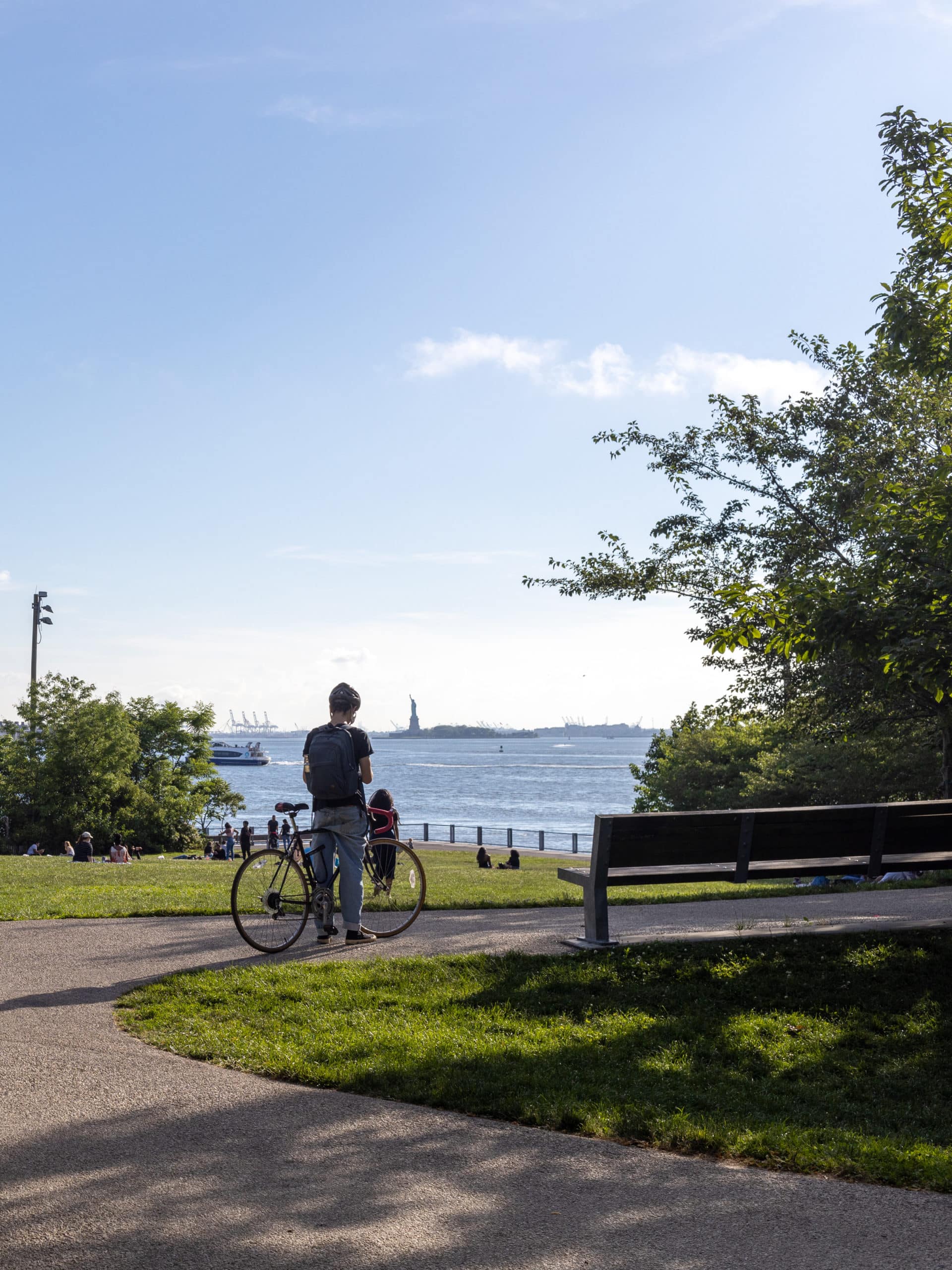 Man with bike on path with view of the Statue of Liberty from Pier 1 on a sunny day.