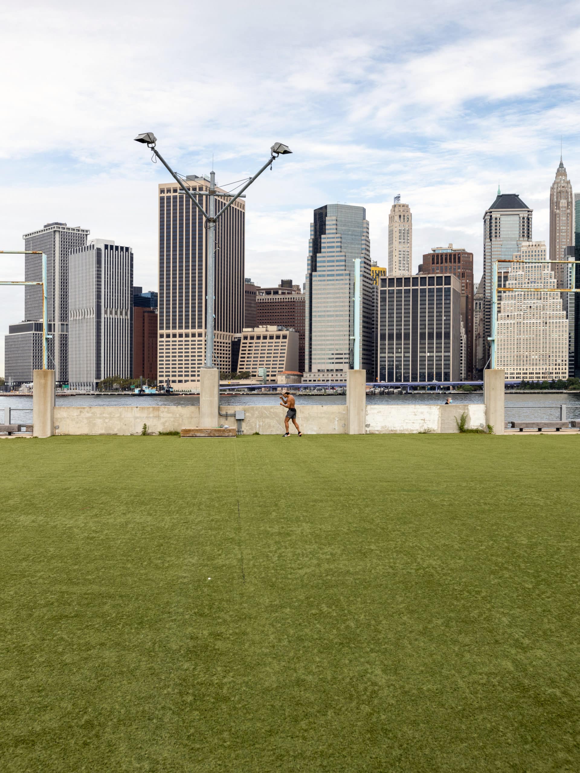 Man exercising on Pier 2 Play Turf on a cloudy day. Lower Manhattan is seen in the background.