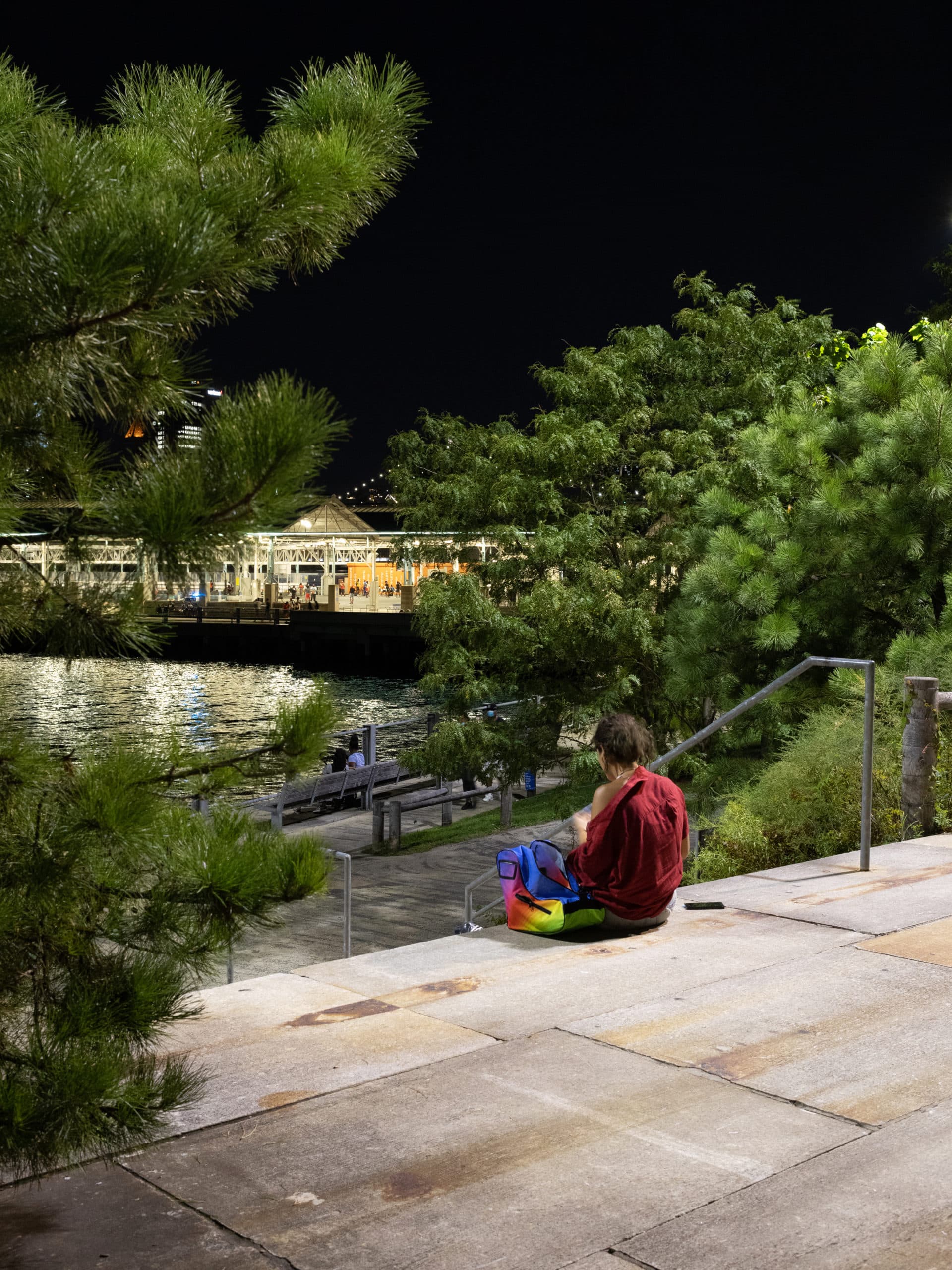 Woman sitting on steps to Granite Terrace at night with Pier 2 in the distance.