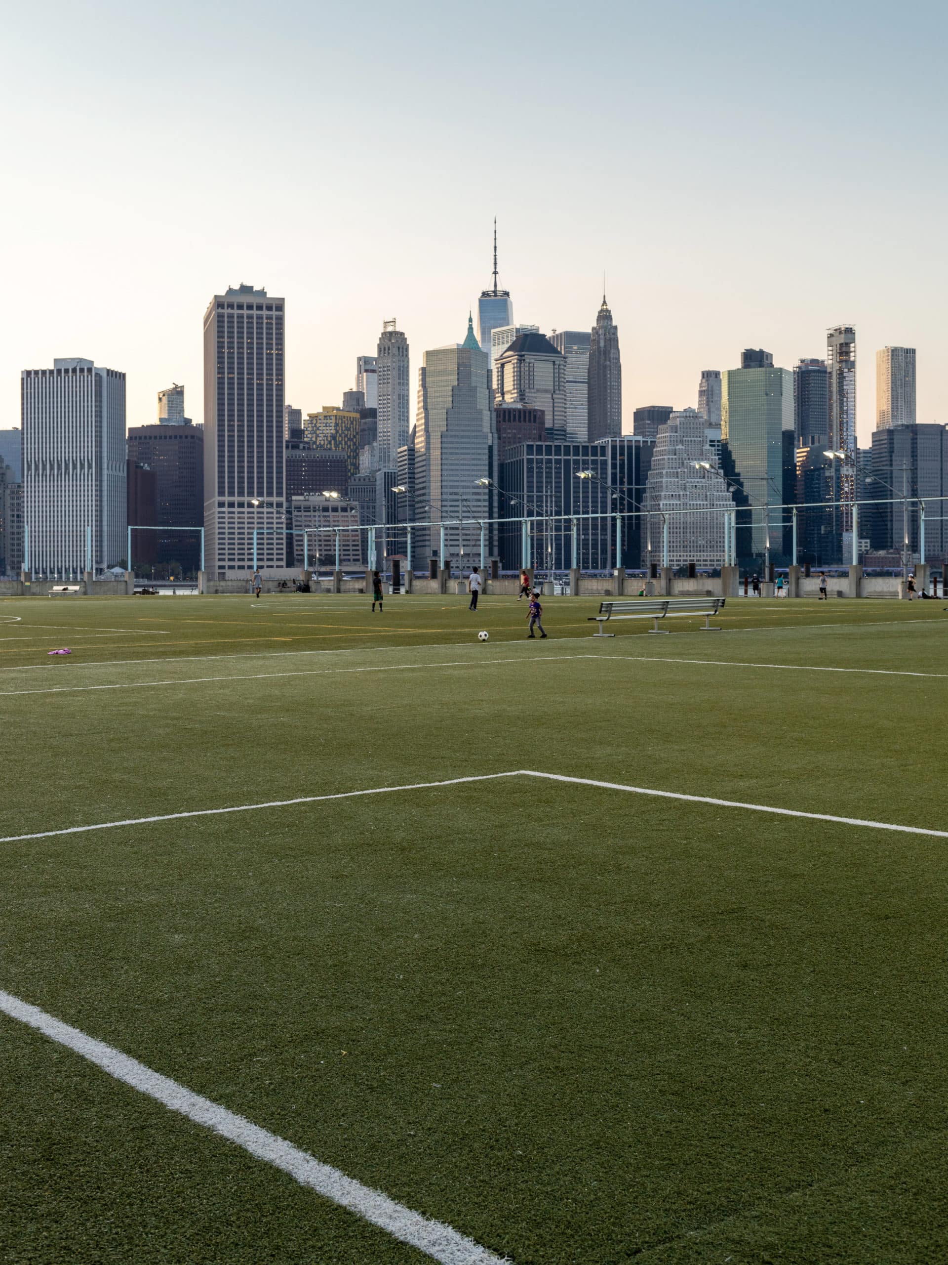 People playing soccer on the Pier 5 Sport Fields at sunset with lower Manhattan in the distance.