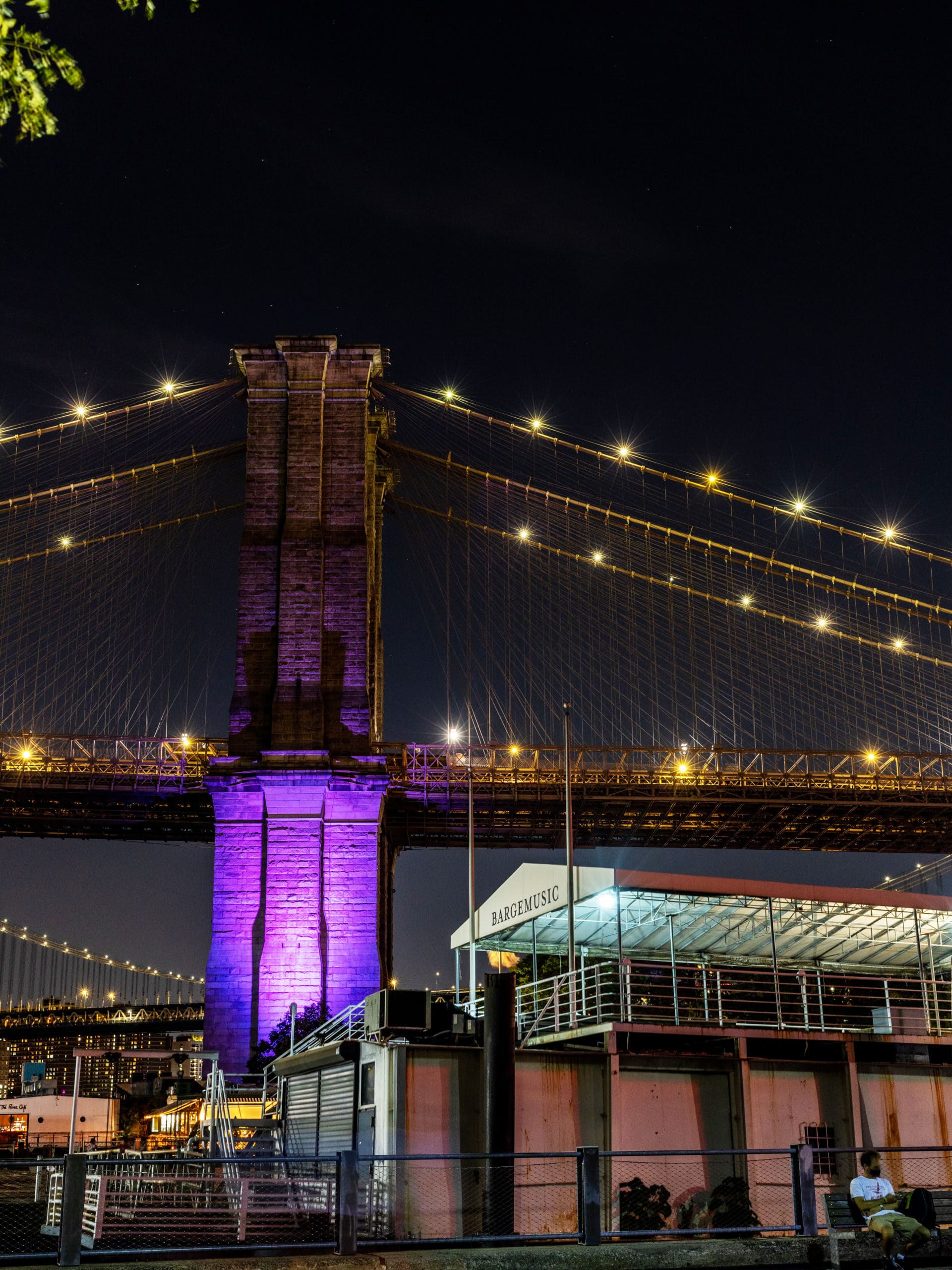 Bargemusic Stage at night. The Brooklyn Bridge is seen behind lit with purple lights.
