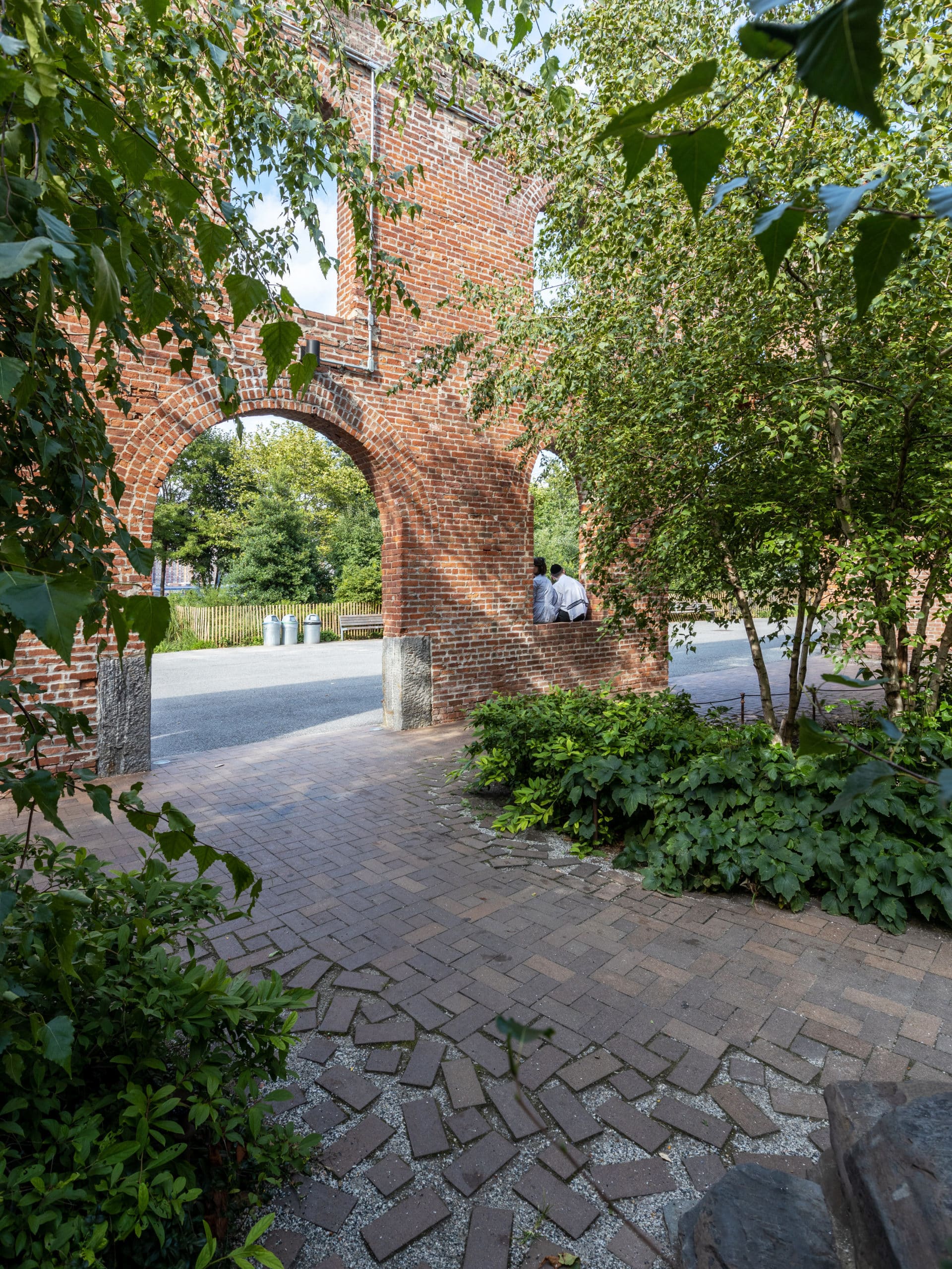 Tree-lined pathway facing the arched brick entrance to Max Family Garden on a sunny day.