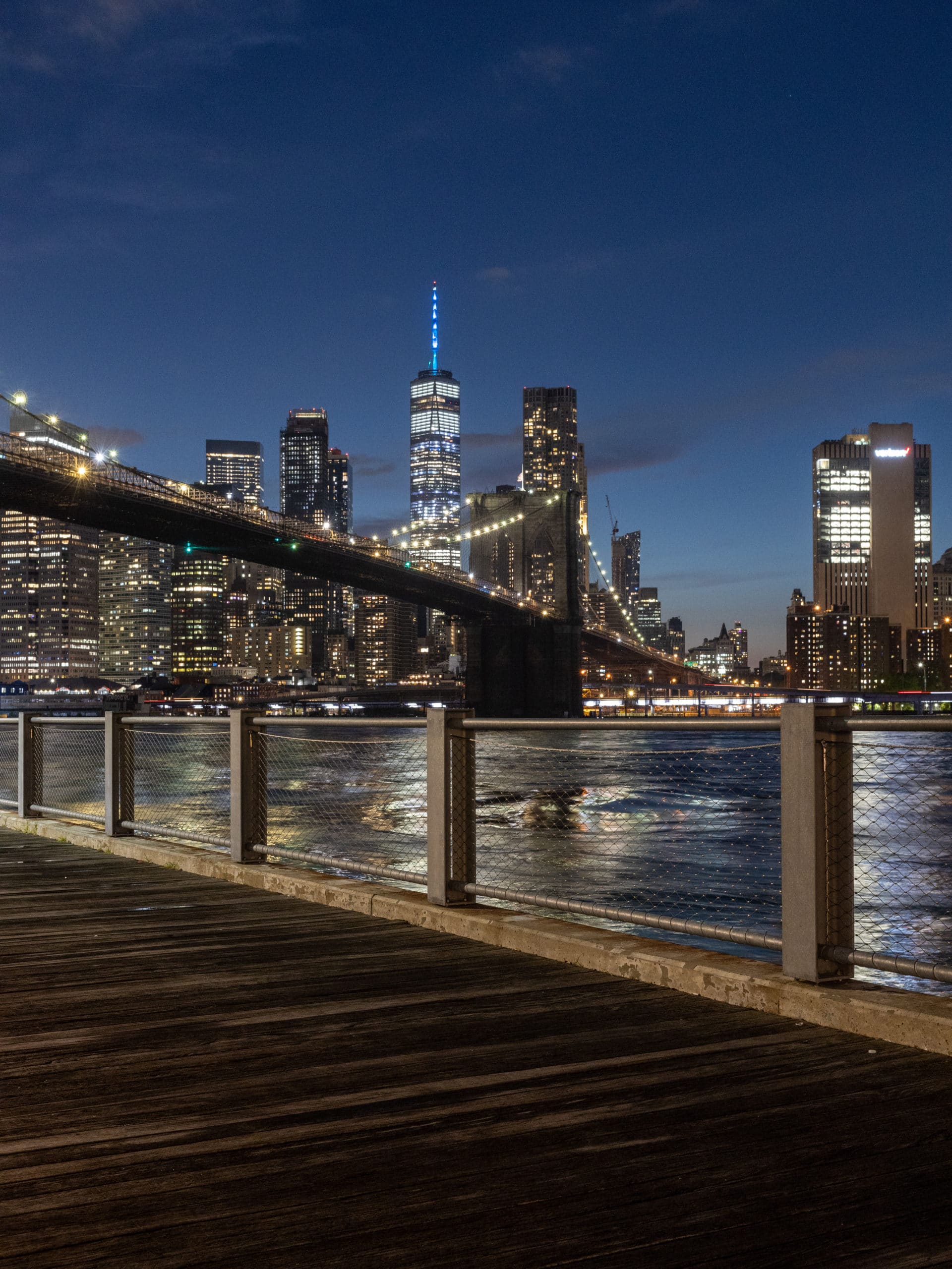 View of the Brooklyn Bridge and Freedom Tower at night from the boardwalk.