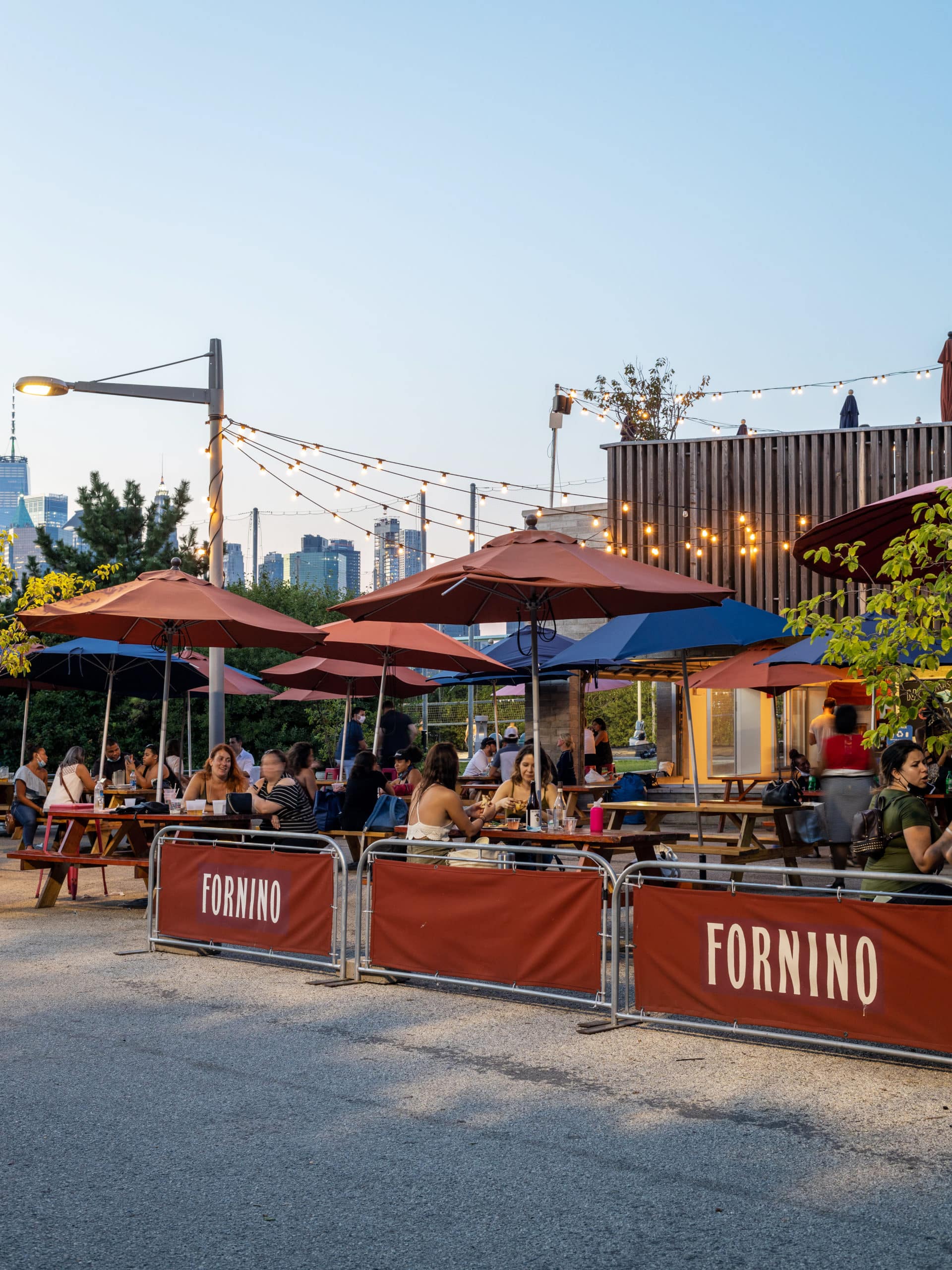 People eating outside under umbrellas at Fornino at sunset.