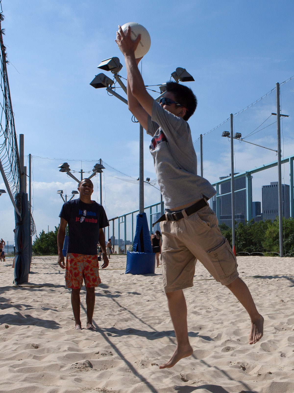 Man catching volleyball on a sand court at Pier 6 on a sunny day.
