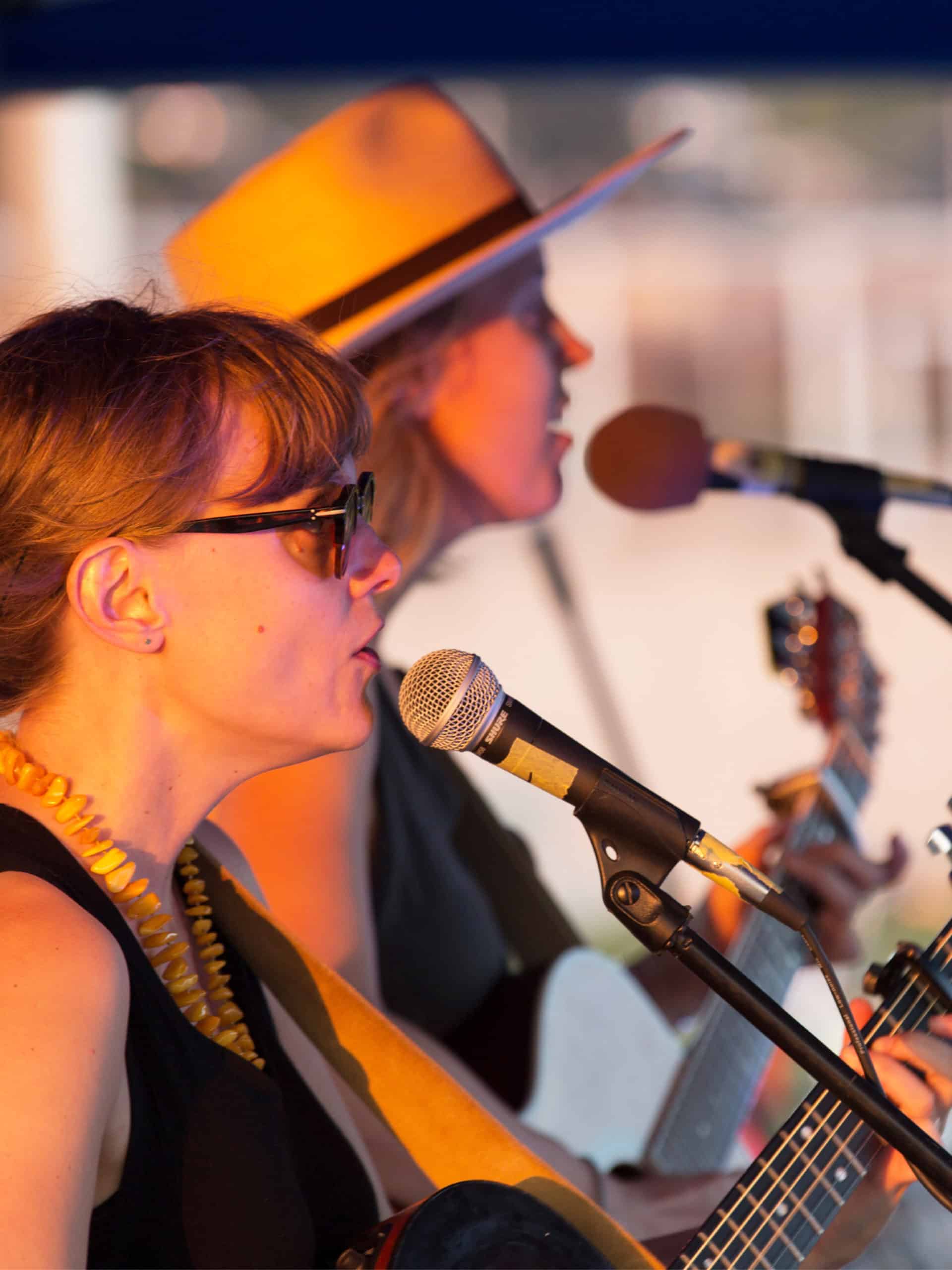 Two women singing into microphones at sunset.