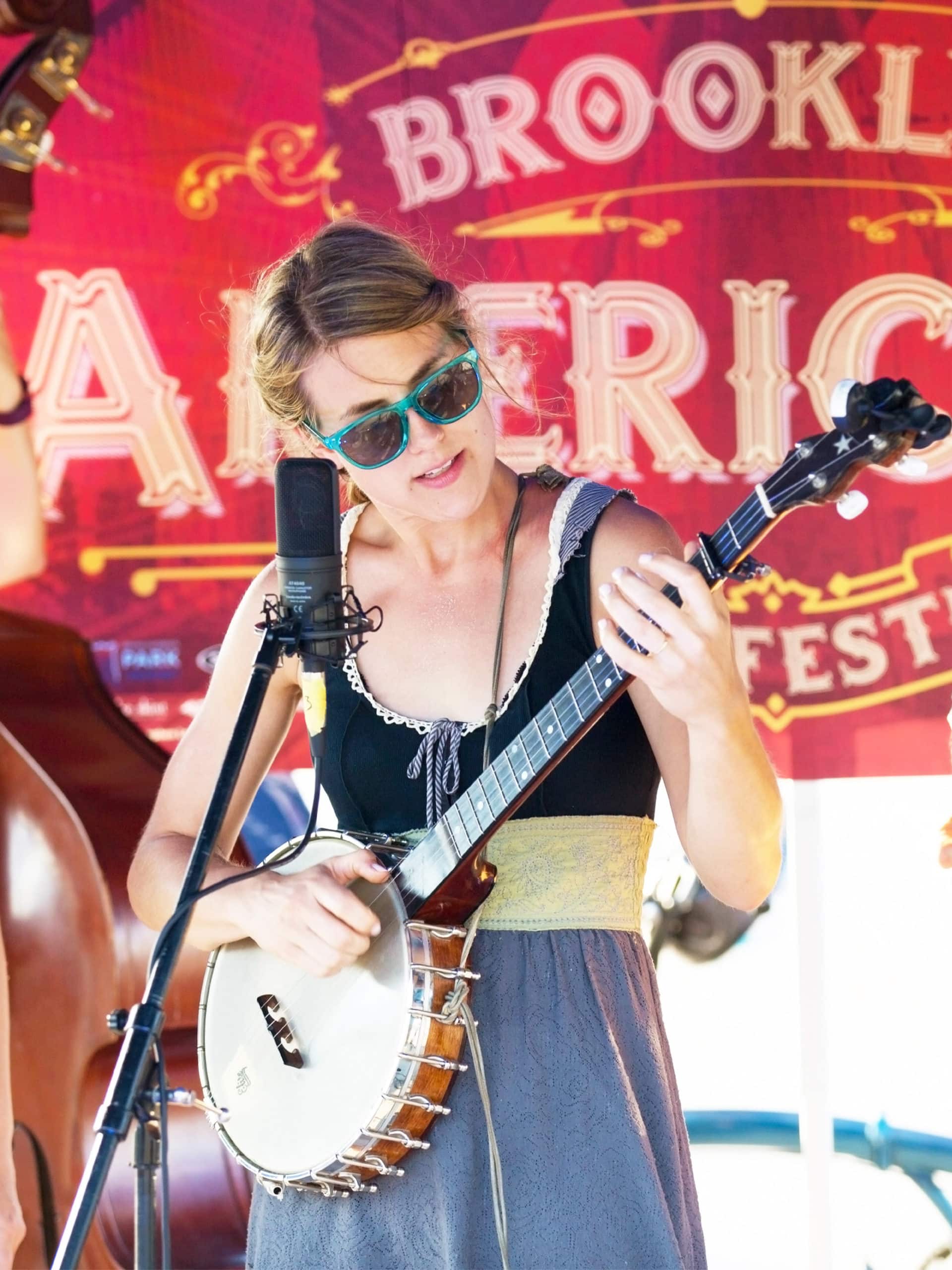 Woman playing a banjo in front of an Americana Festival banner.
