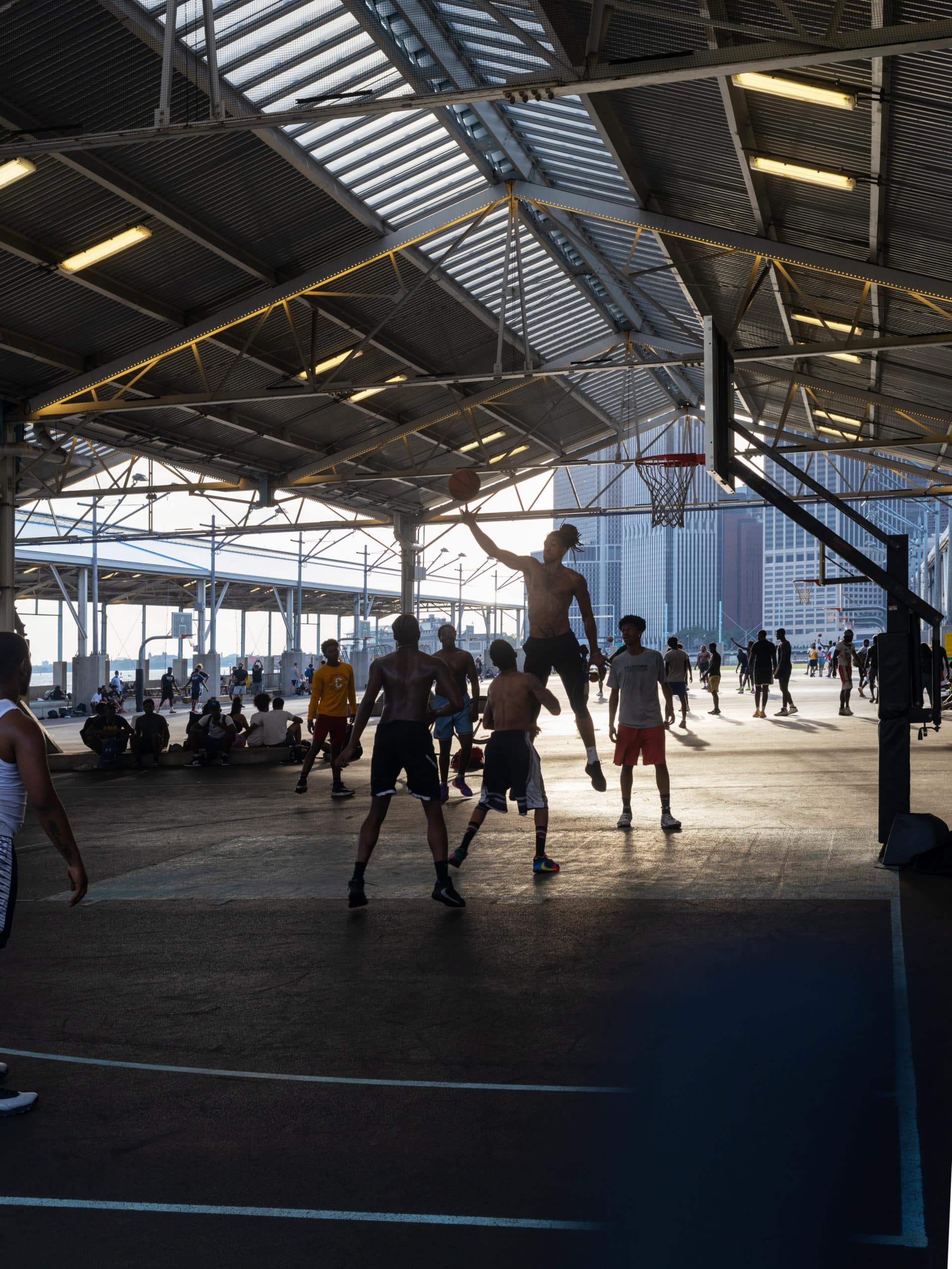 Man jumping with basketball during a game under the canopy at Pier 2. Other basketball games are being played in the background.