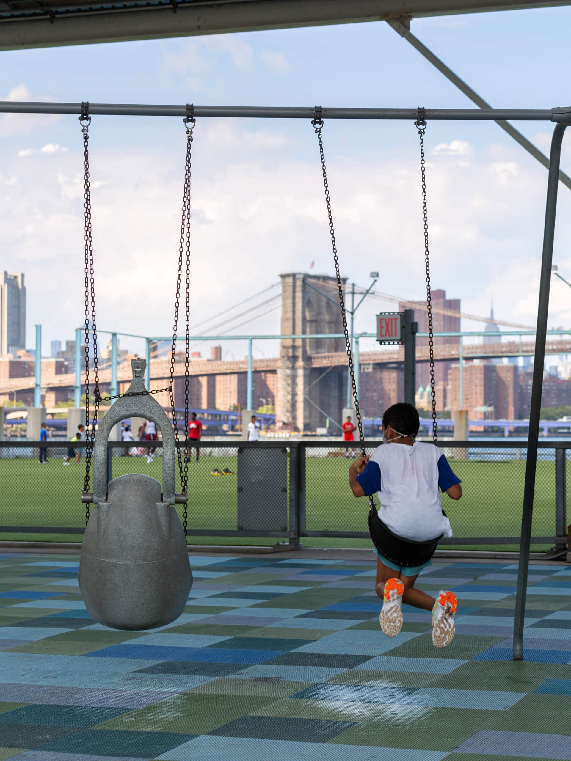 Boy swinging on the swings at Pier 2 with the Brooklyn Bridge in the distance.