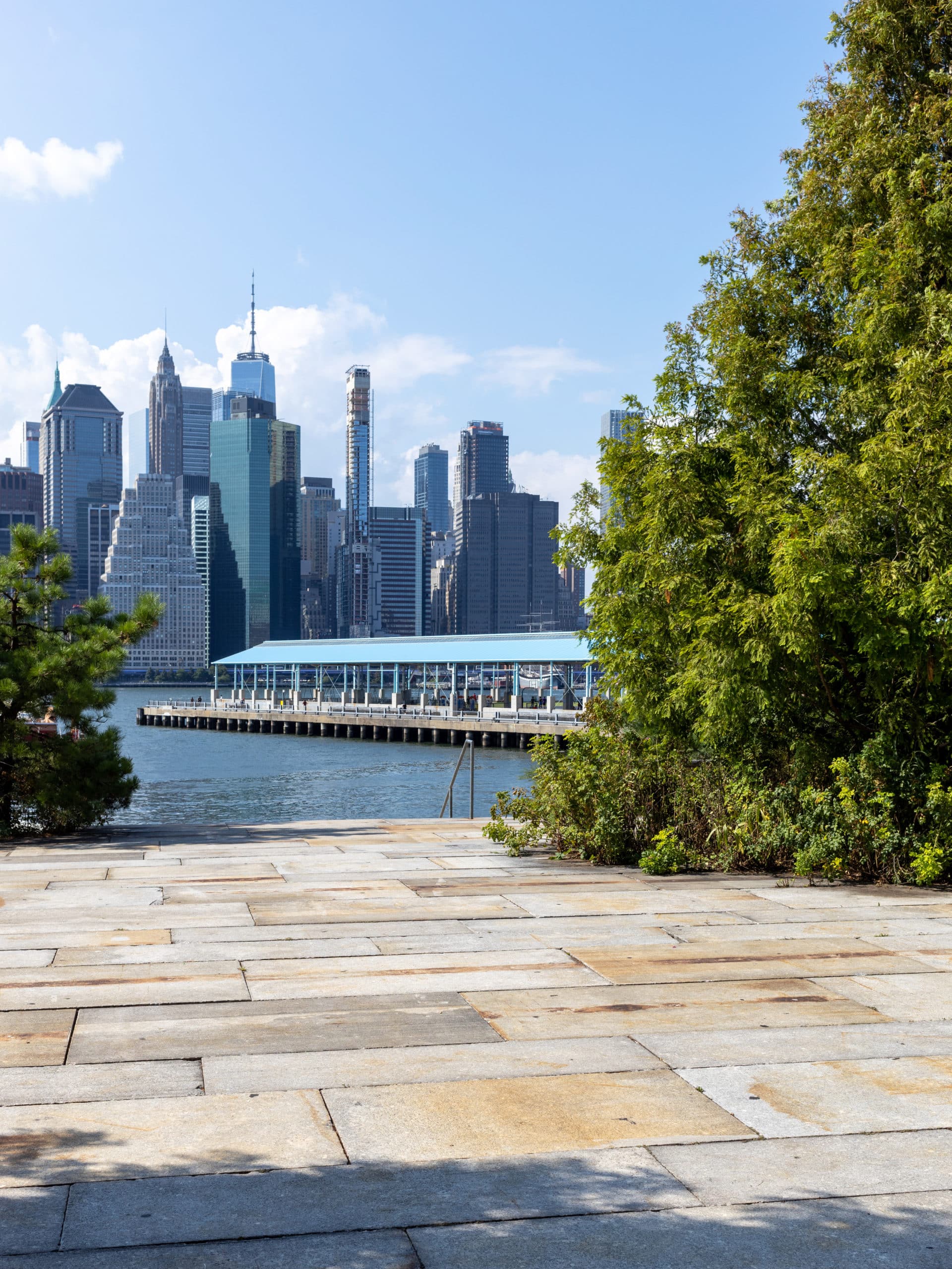 Stone terrace looking out over the water with a view of Pier 2 and lower Manhattan on a sunny day.