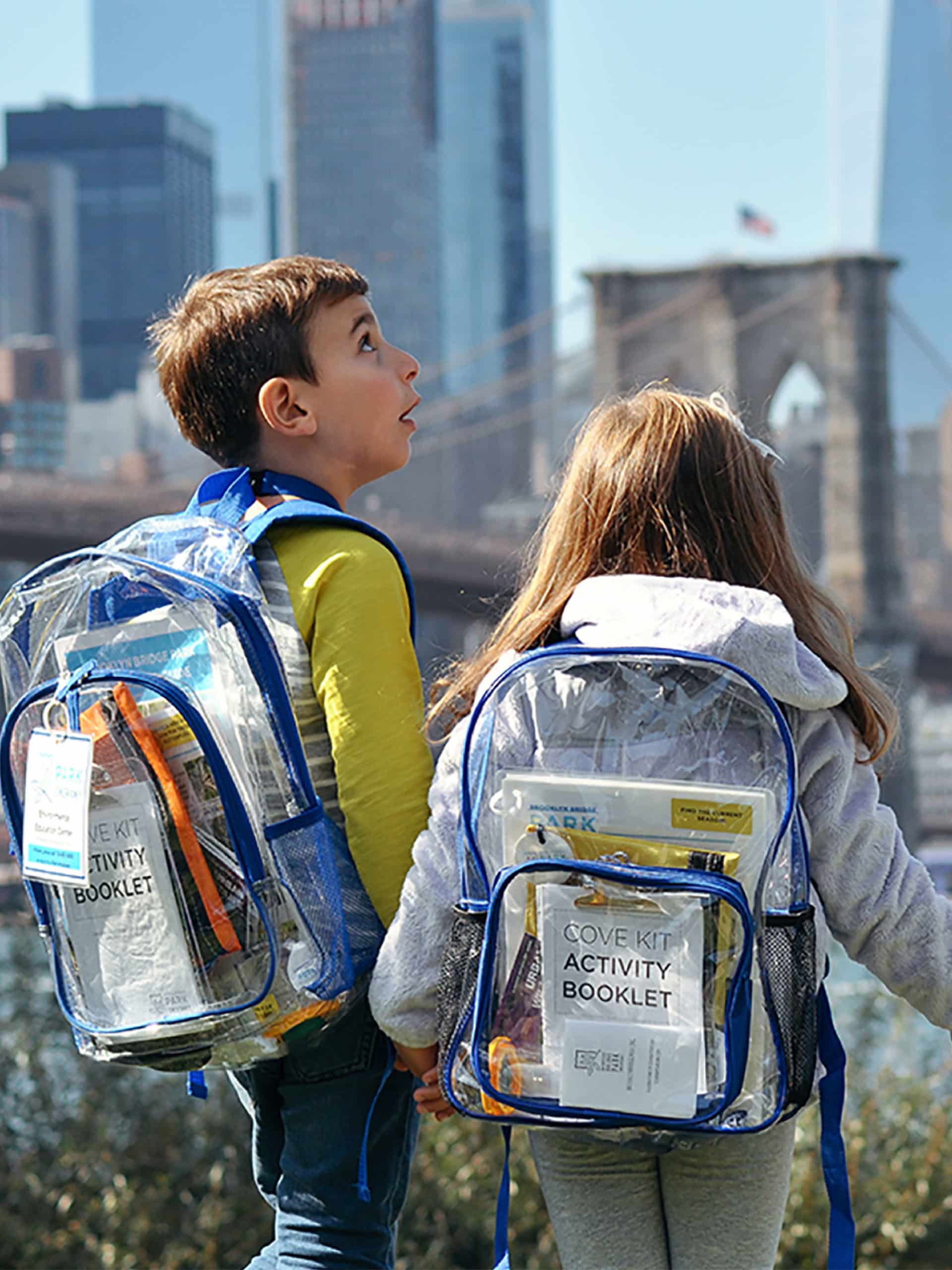 Two children holding hands with Cove Kit backpacks on.