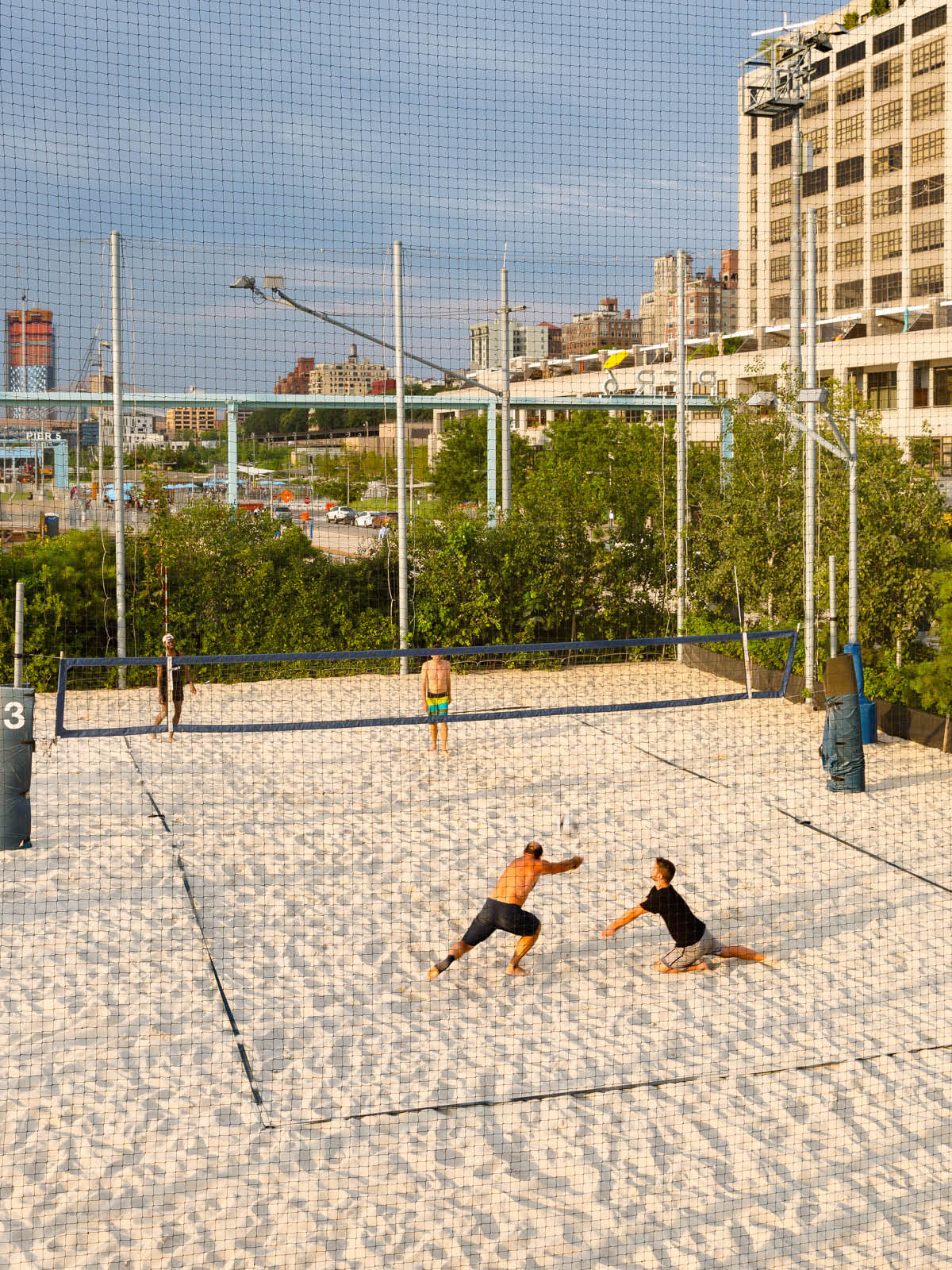 Two men diving for a ball during a volleyball game at Pier 6 courts at sunset.