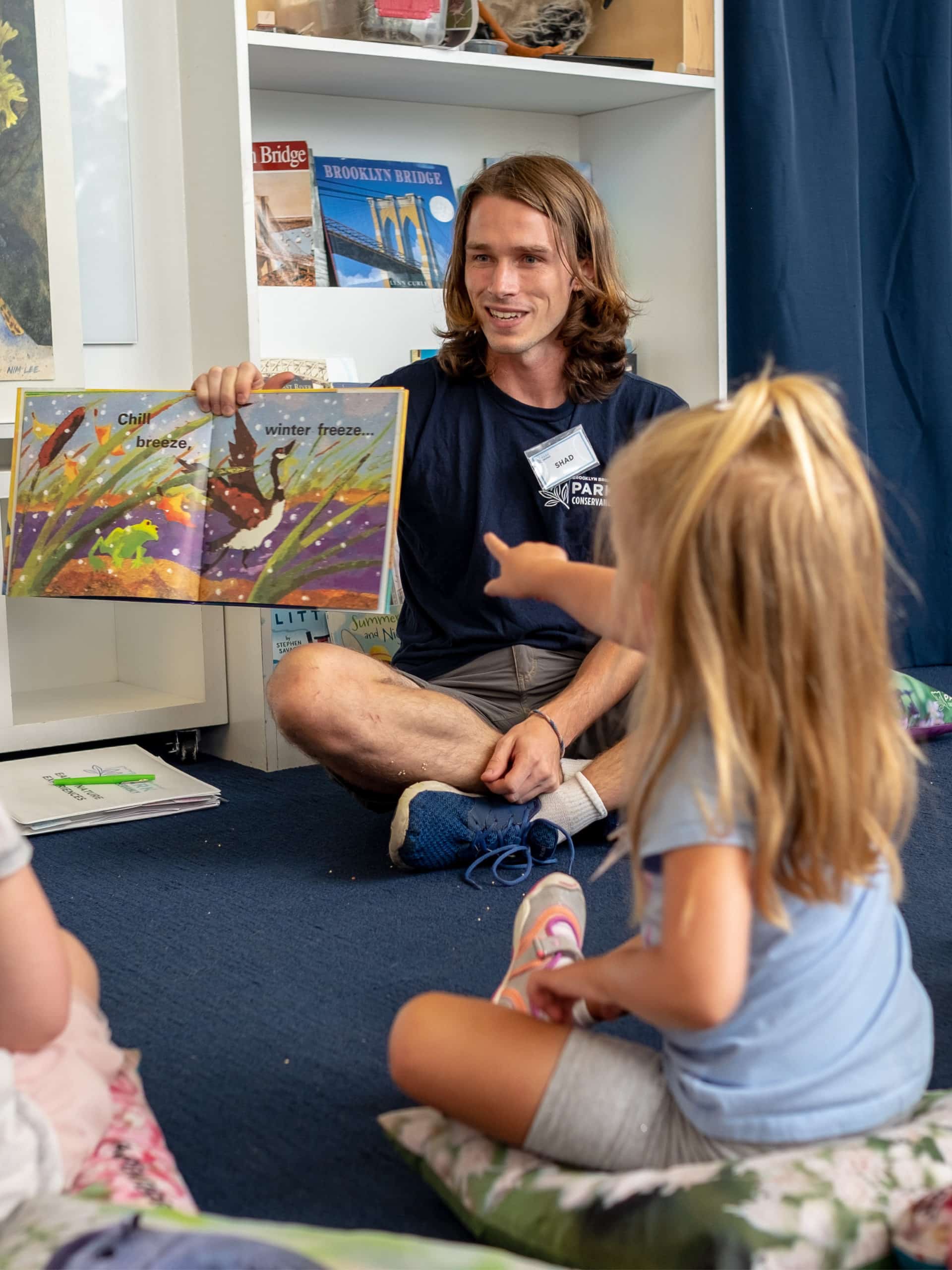 Instructor reading from a book to small children in a classroom.