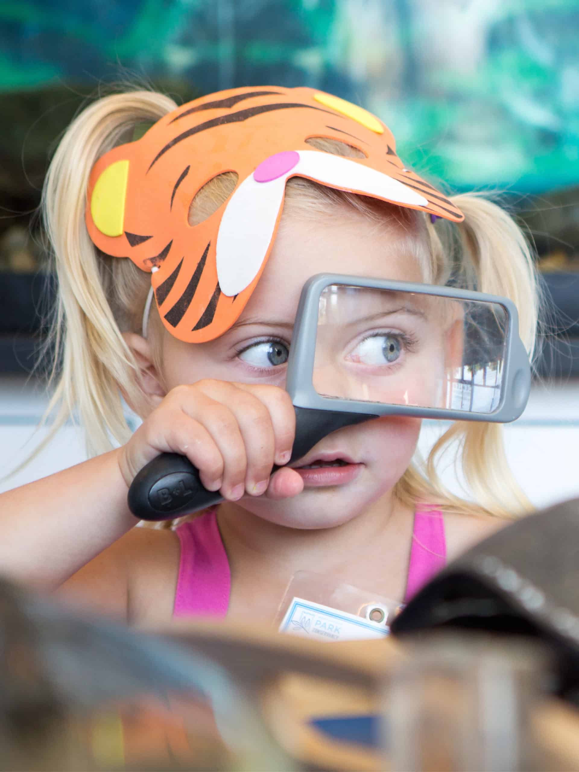 Girl in a tiger mask holding a magnifying glass.