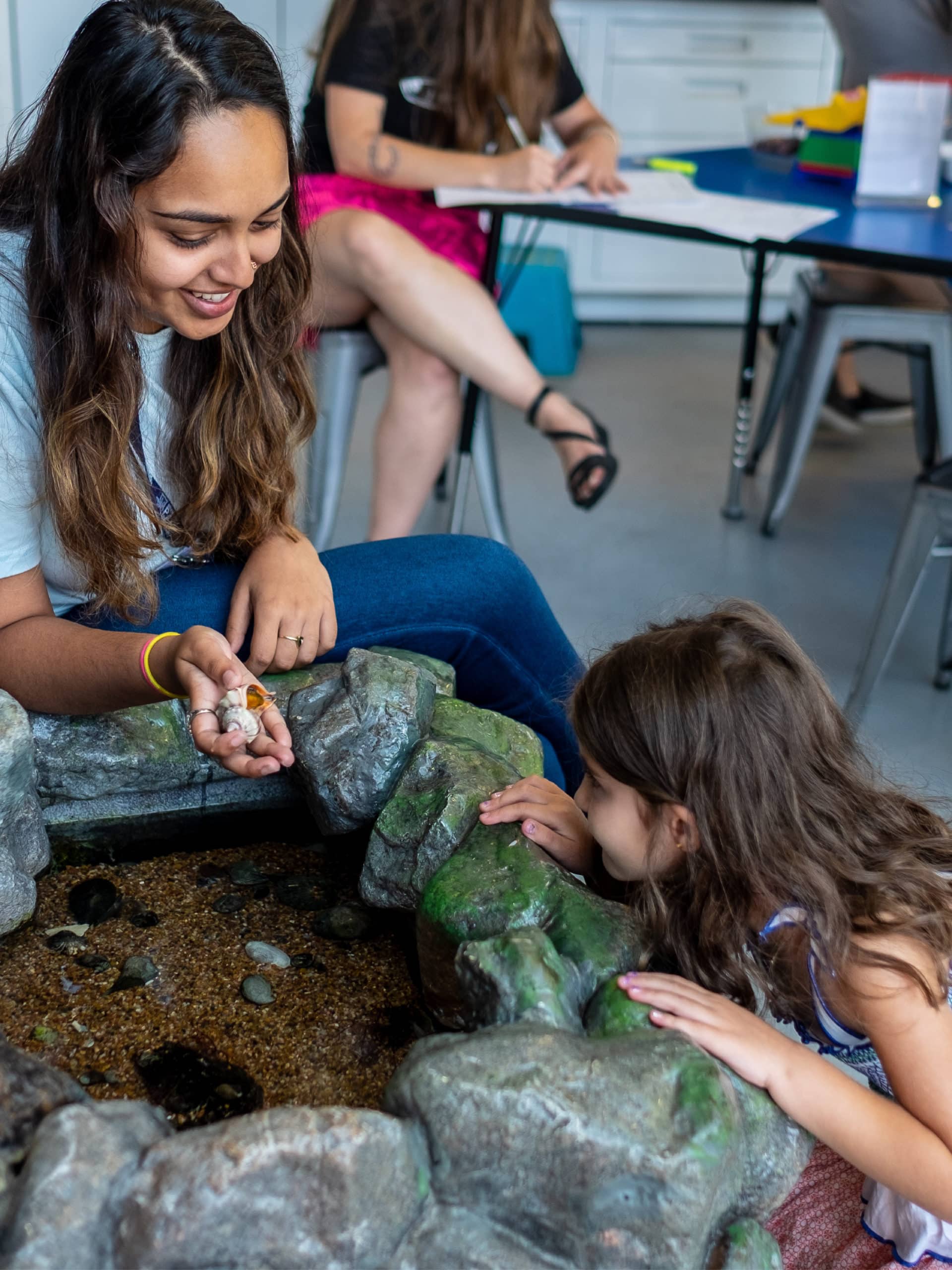 Girl looking at hermit crab held by instructor in a classroom.