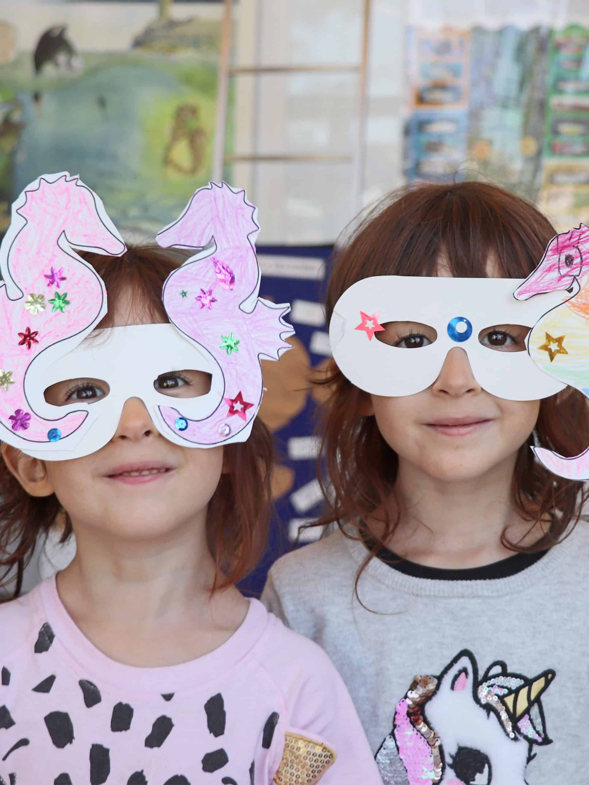 Two girls in paper masks in a classroom.