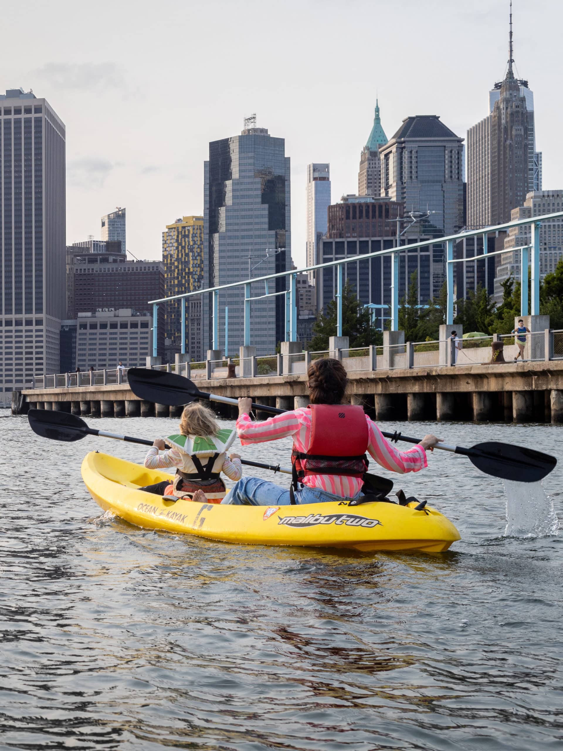 Woman and child paddling away in a yellow kayak with a pier seen in the background.