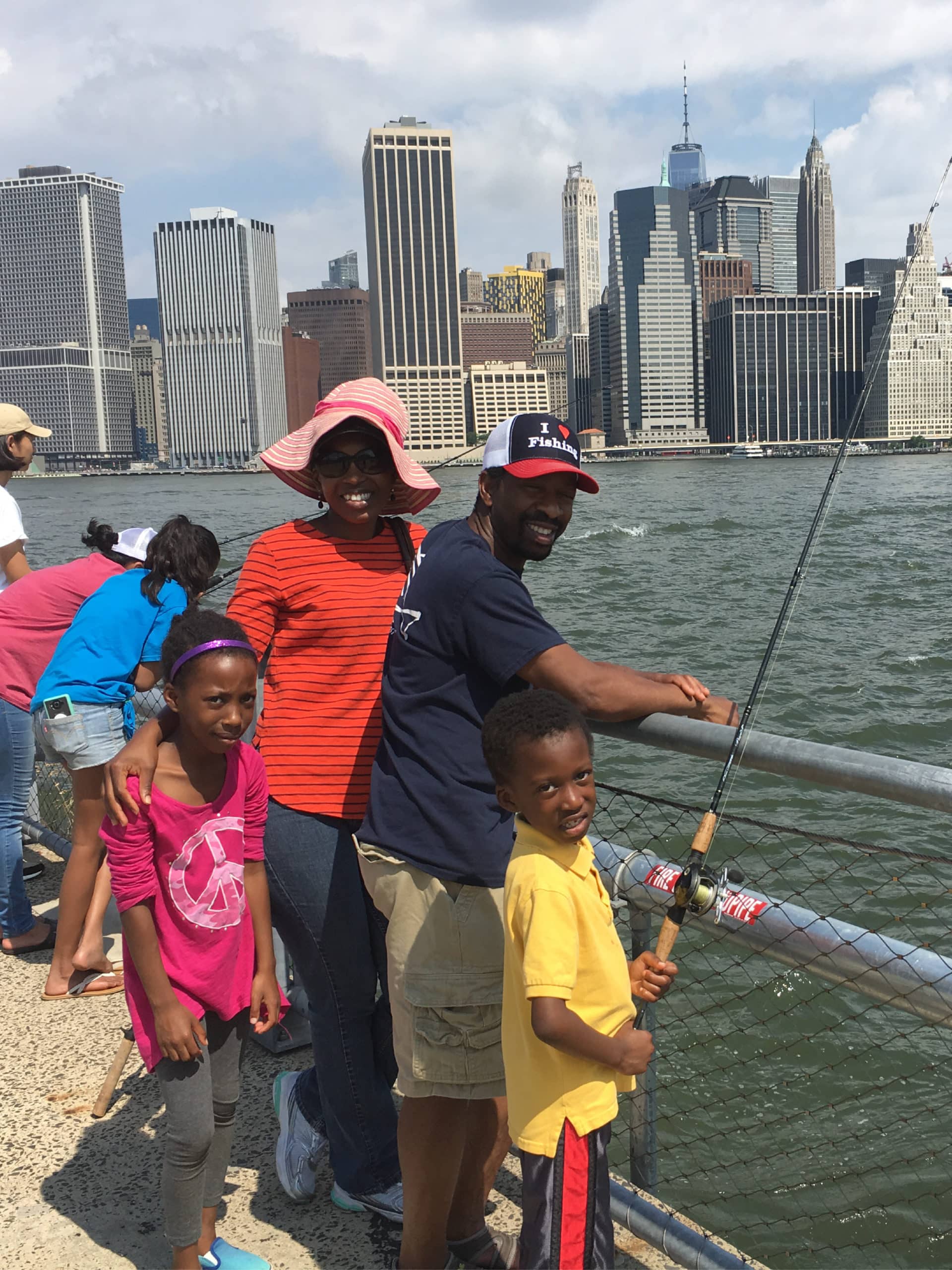 Family smiling and posing with fishing rods by the railing on the promenade.