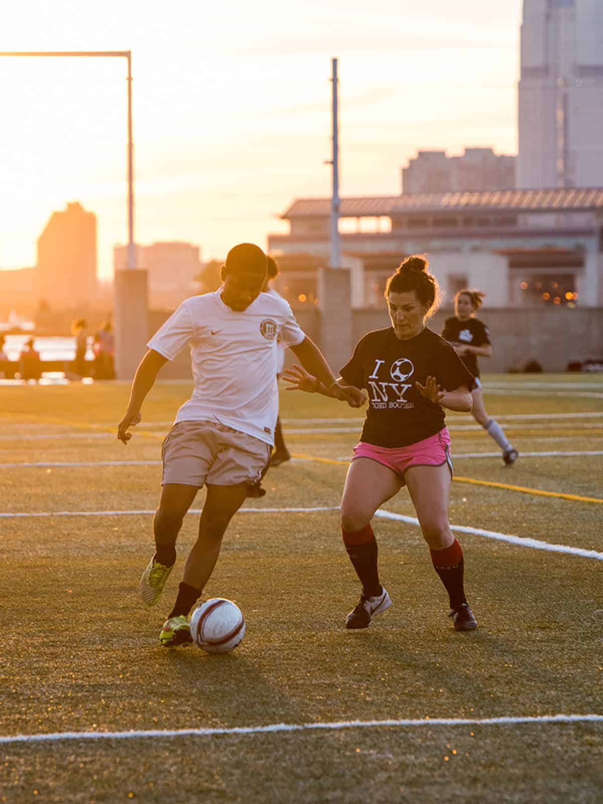 Two people playing soccer at sunset.