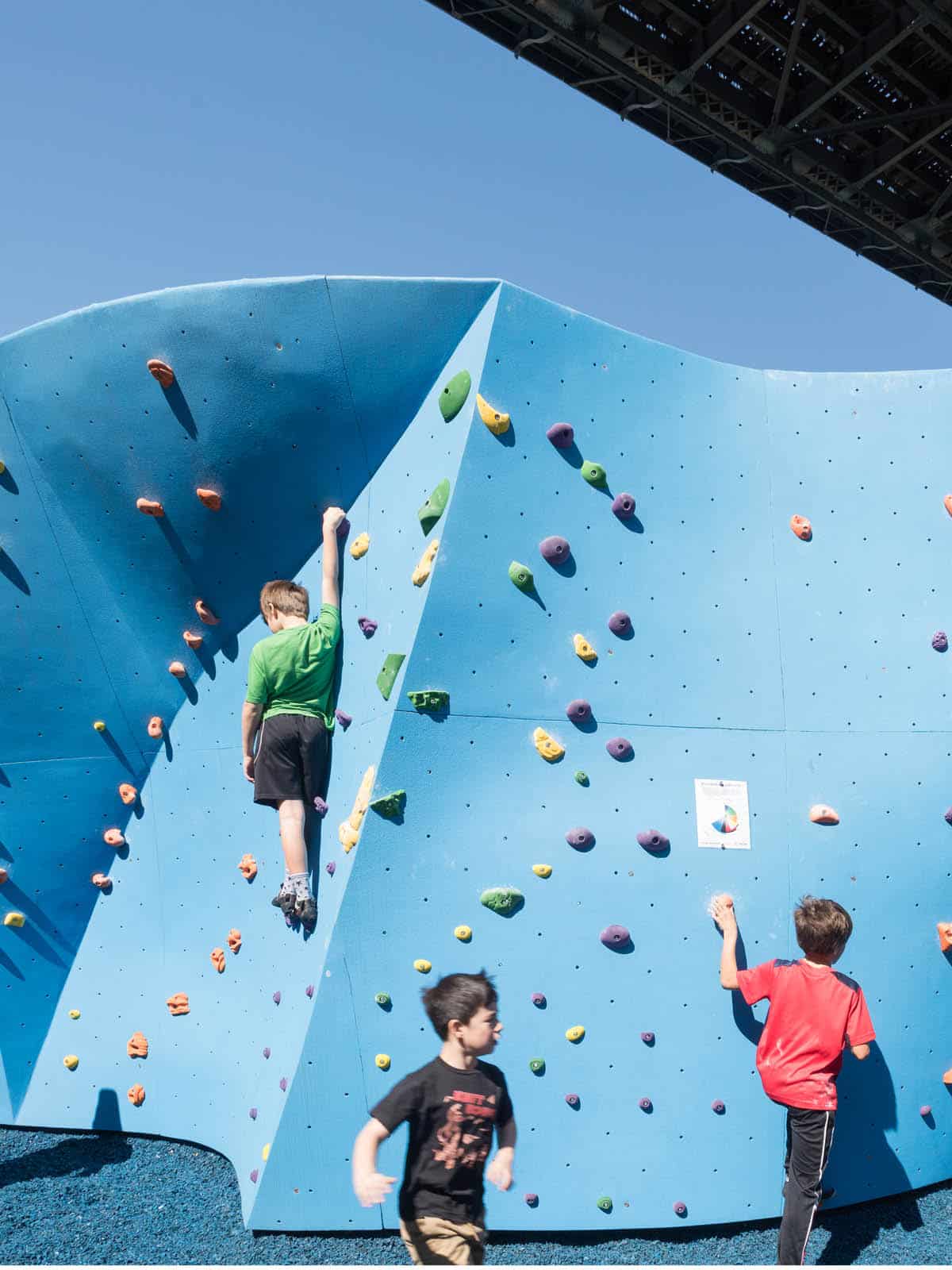 Children climbing a bouldering wall on a sunny day.