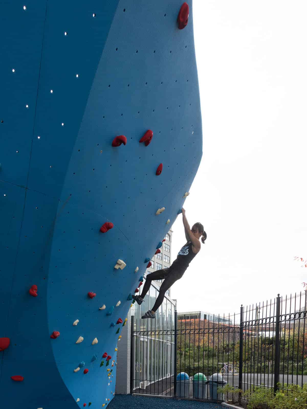 Woman climbing a bouldering wall on a cloudy day.