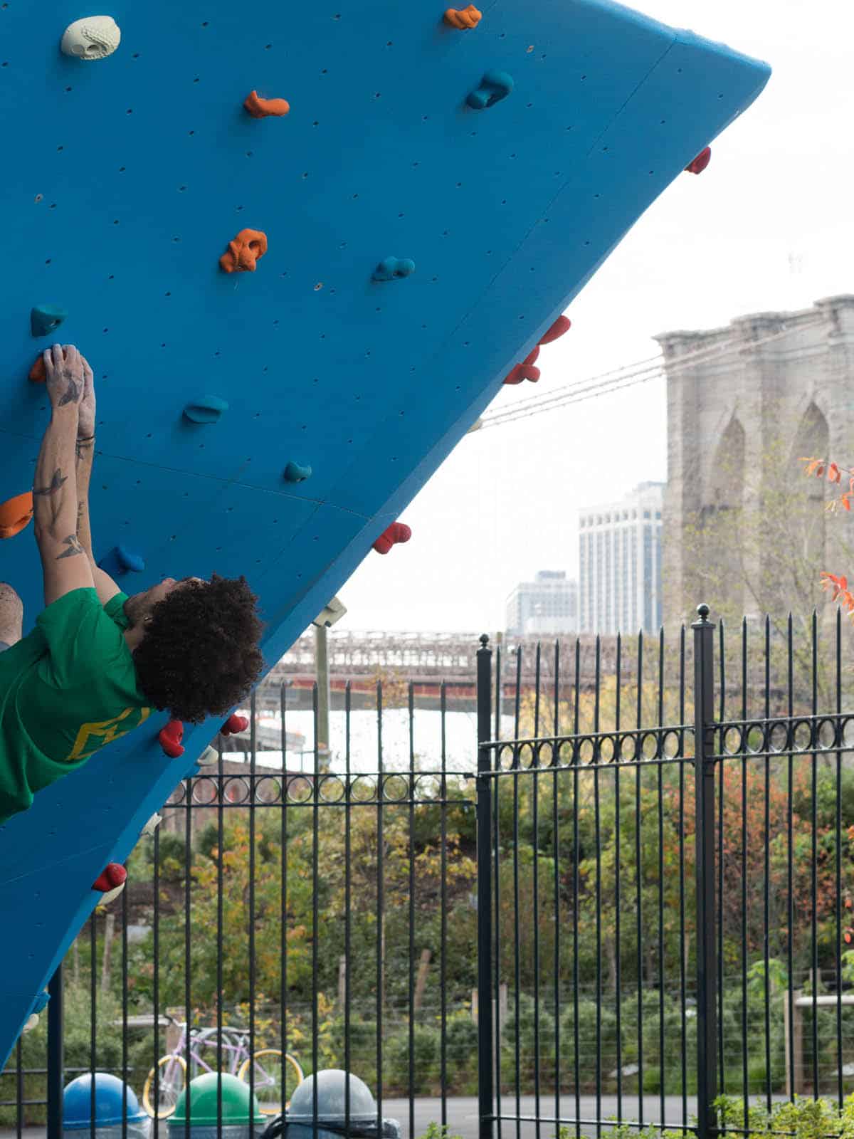 Man climbing in bouldering wall with the Brooklyn Bridge in the background.