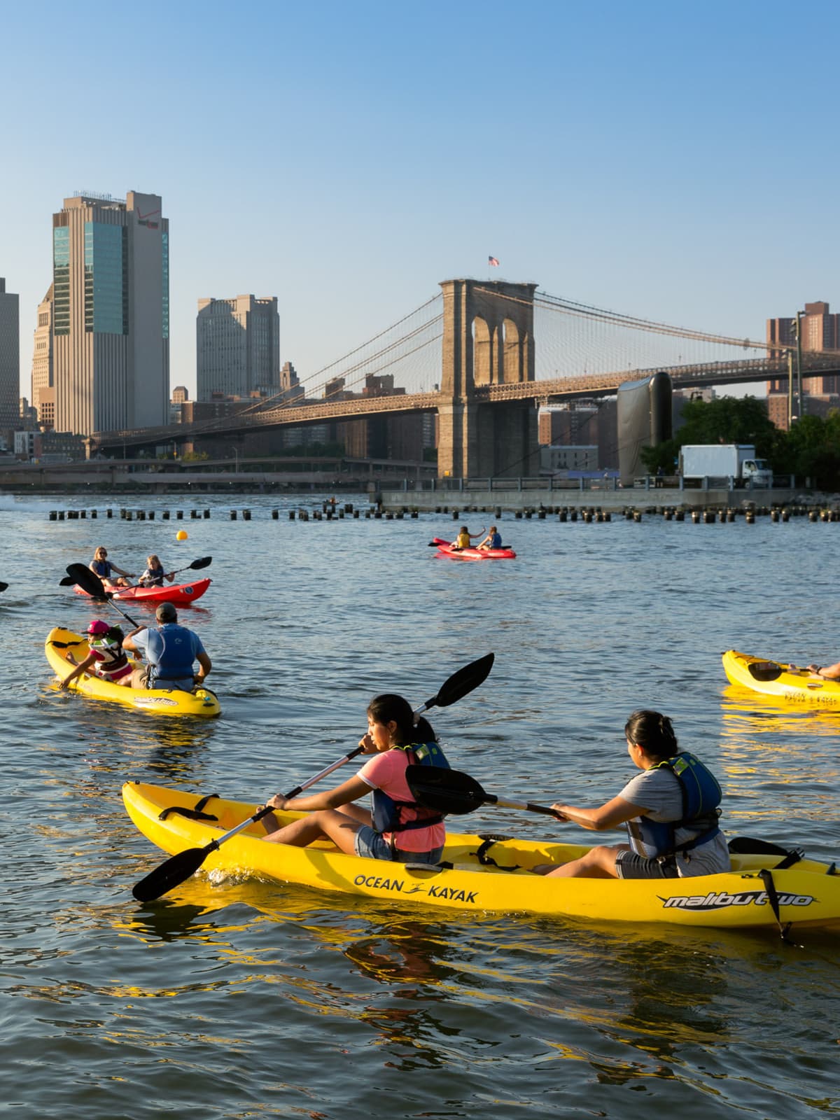 Groups kayaking at sunset with Pier 1 Salt Marsh and the Brooklyn Bridge in the background.