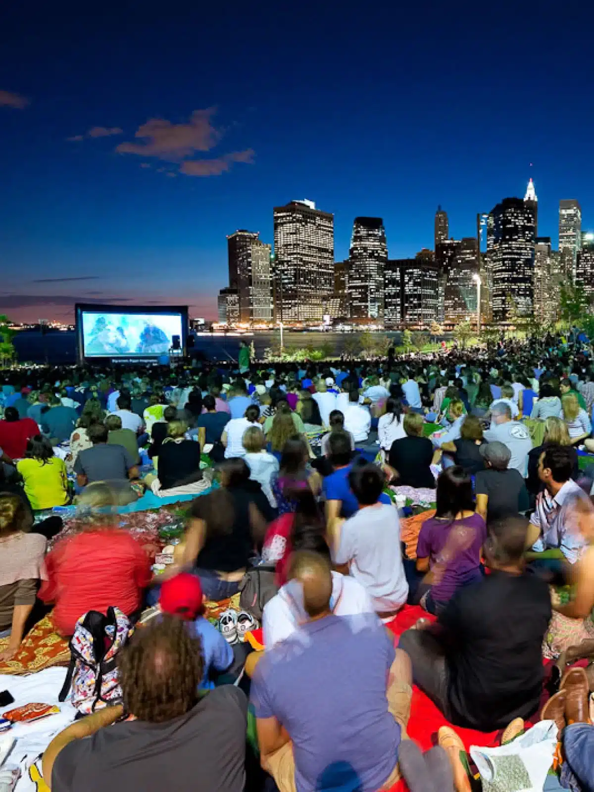 Crowd sitting on the lawn watching a movie on Pier 1 at night. Lower Manhattan is seen in the distance.