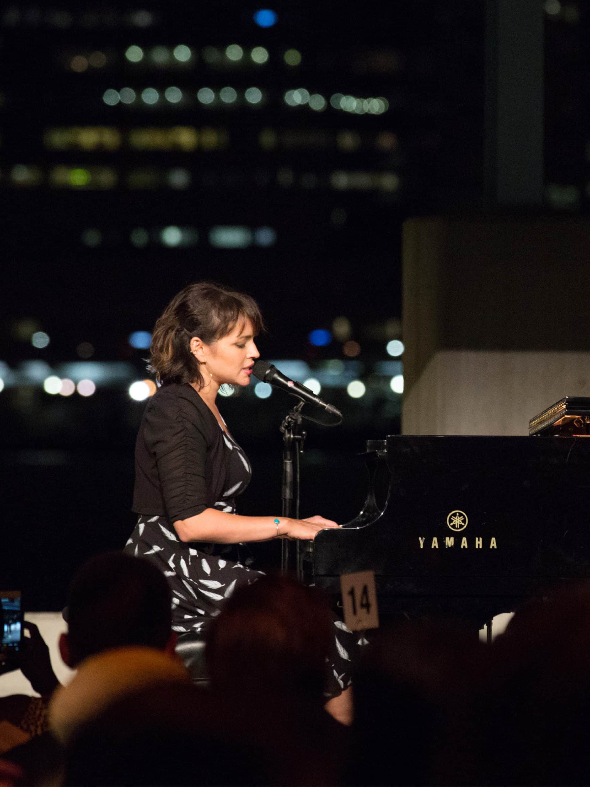 Norah Jones performing at a piano at the Brooklyn Black Tie Ball at night.