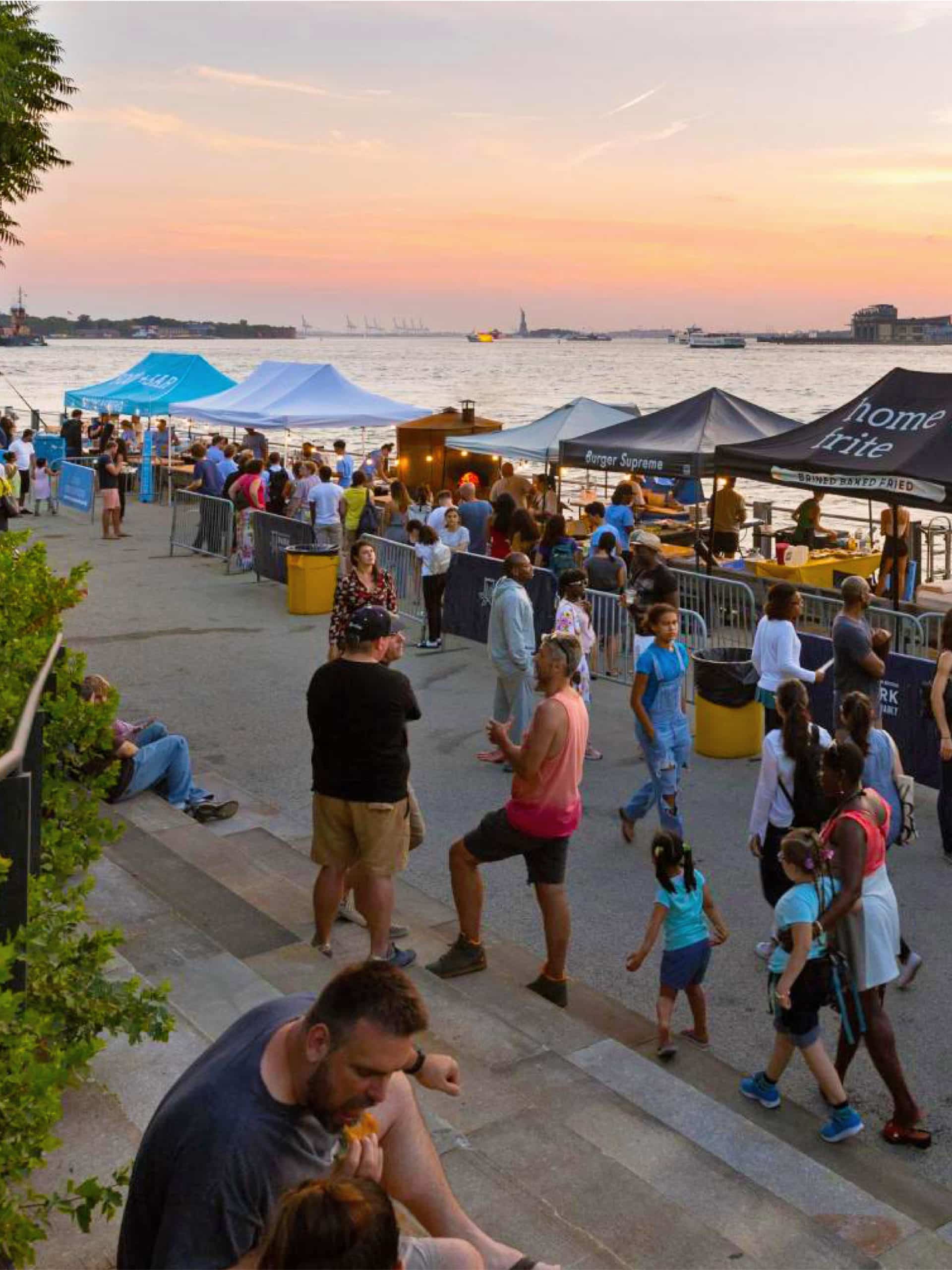 People walking through food stalls on the Pier 1 Promenade at sunset.