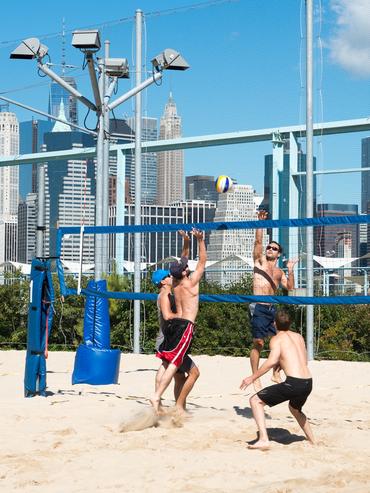 Men playing volleyball on a sand court on a sunny day.