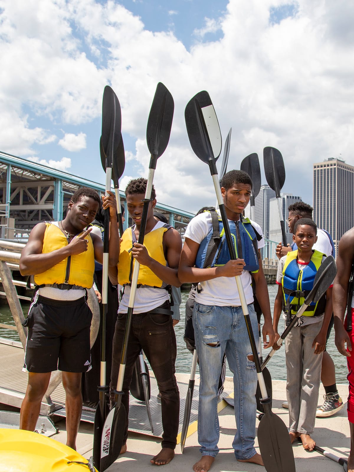 Group of teens holding kayak paddles on the dock on a sunny day.