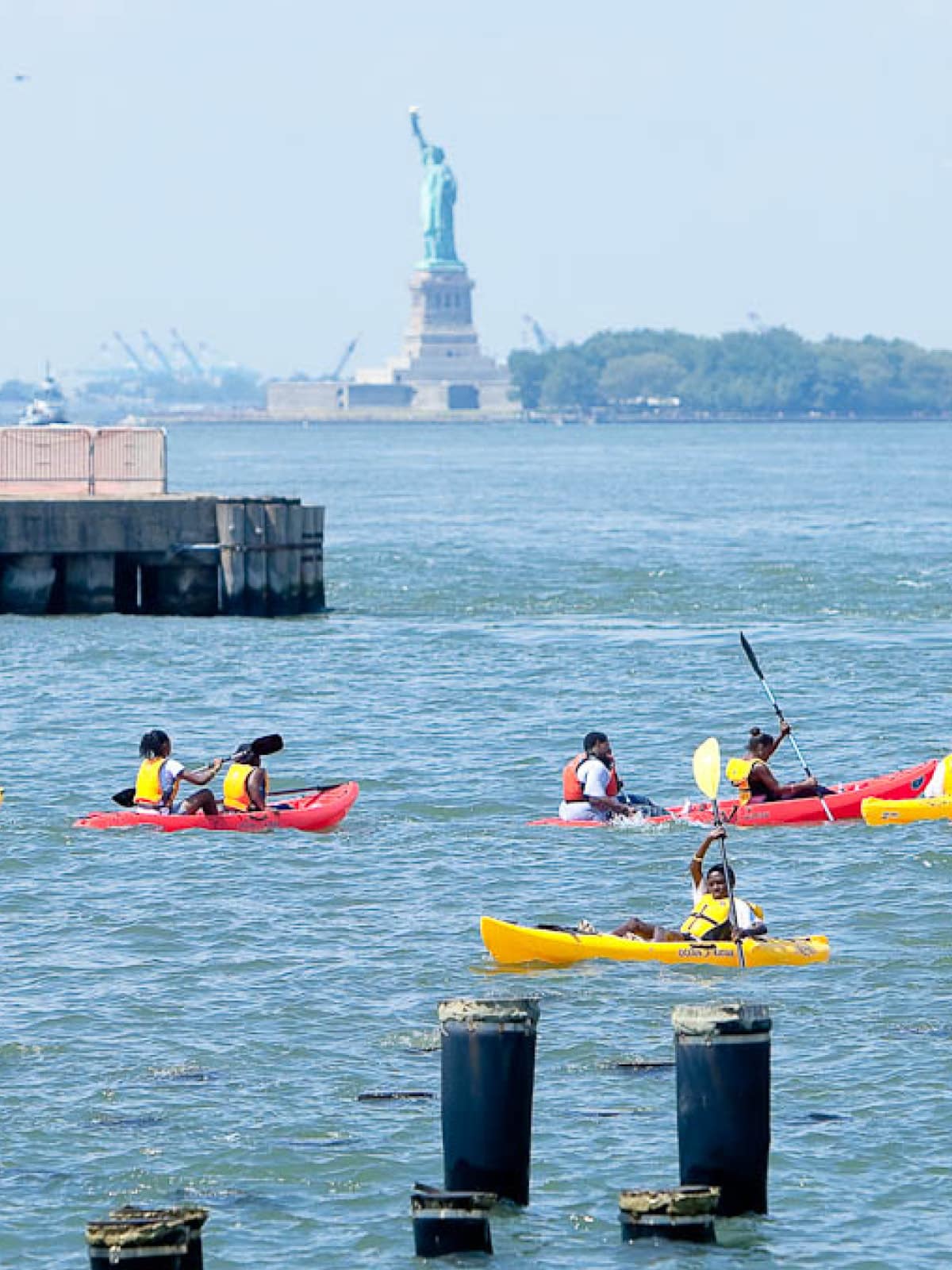 People in kayaks with the Statue of Liberty in the background.