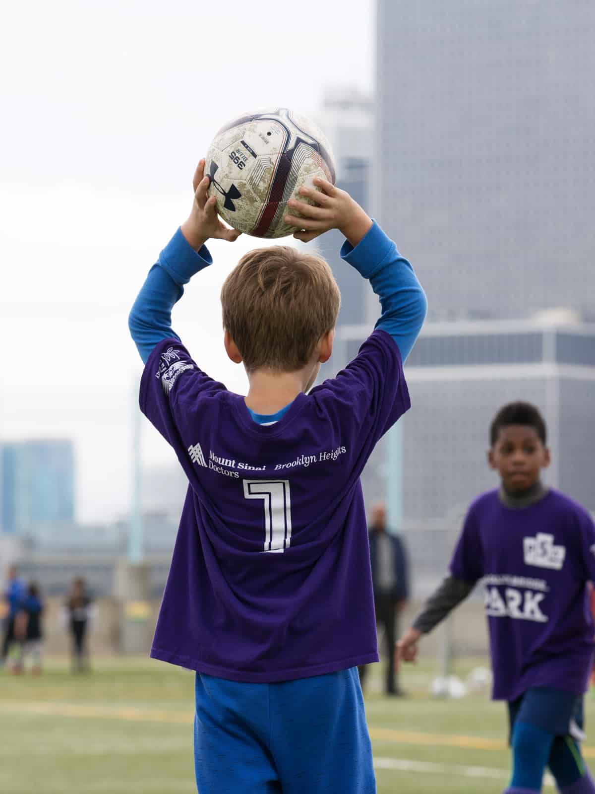 Young boy holds a soccer ball over his head on a cloudy day.