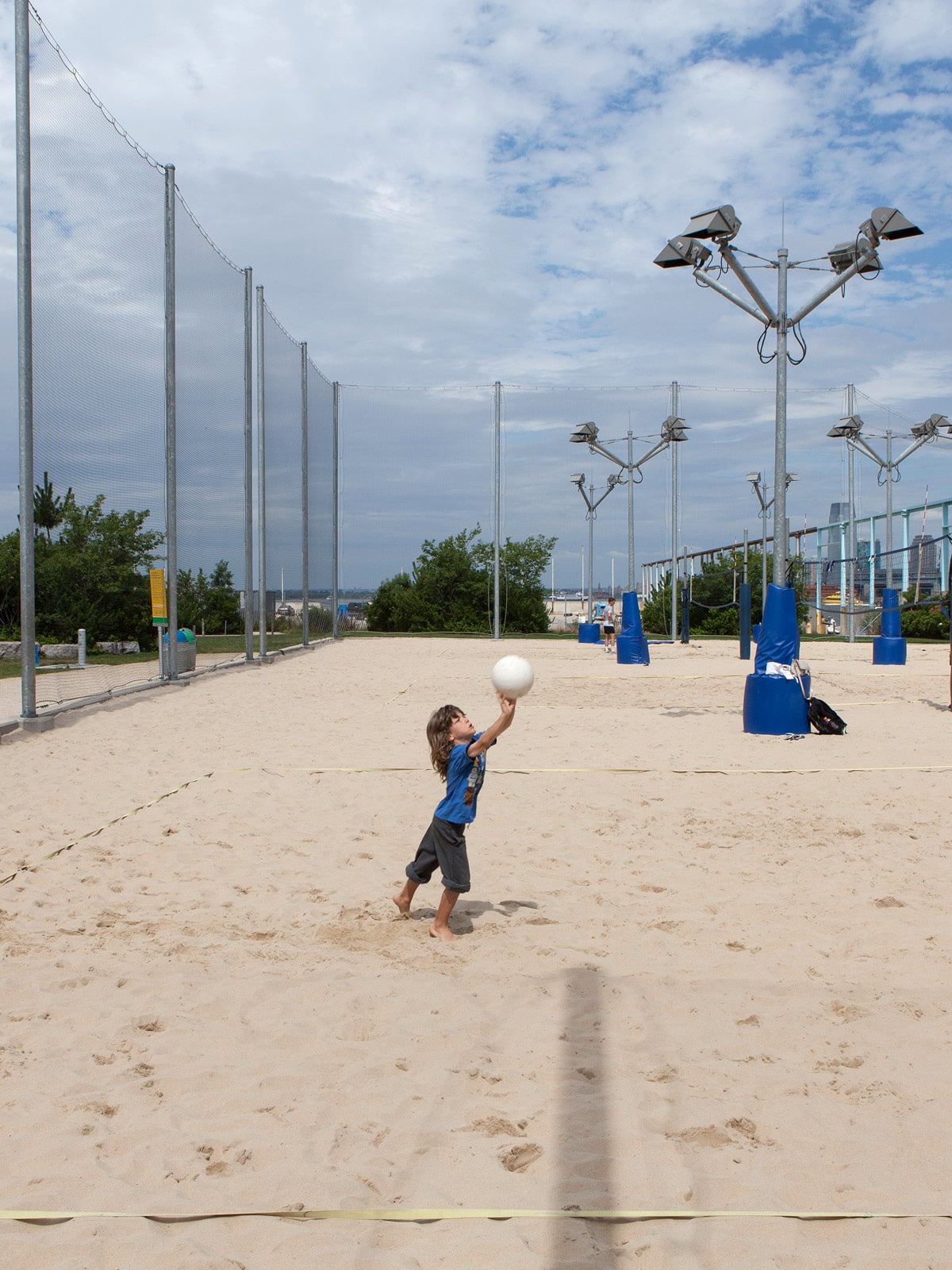 Small child hitting volleyball on a sand court at Pier 6 on a sunny day.