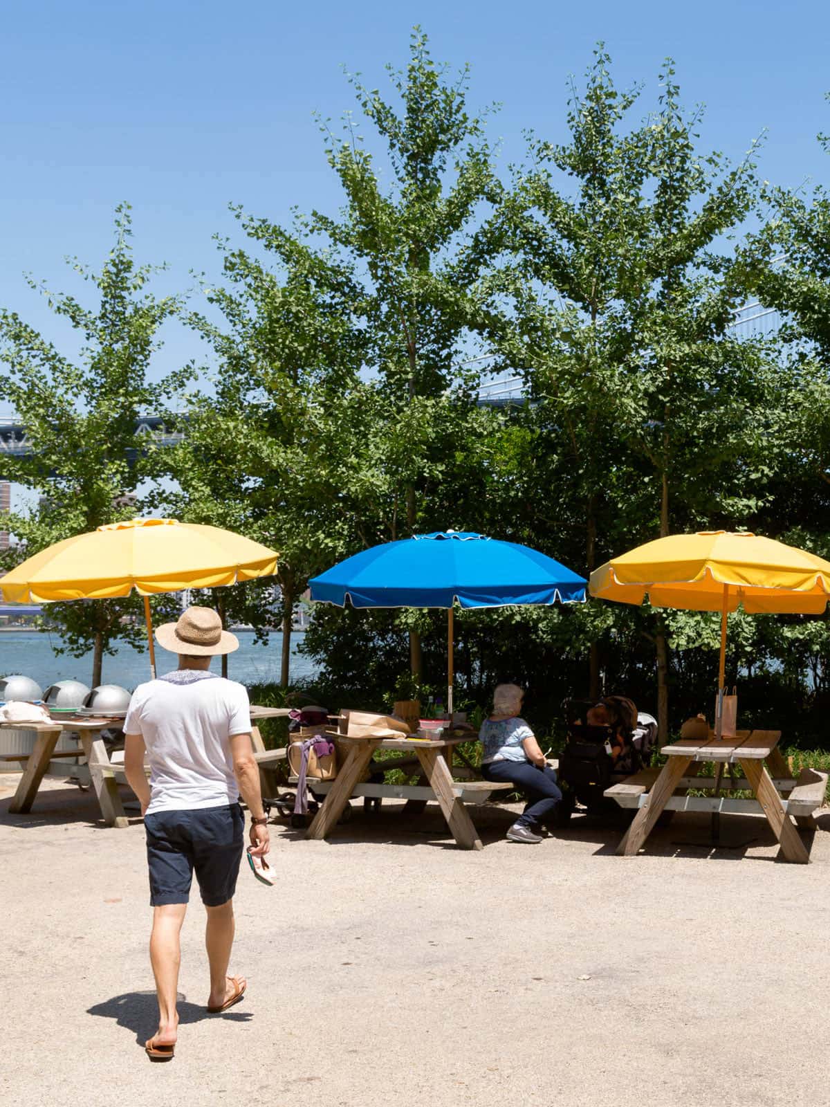Man walking towards picnic tables under umbrellas on a sunny day.