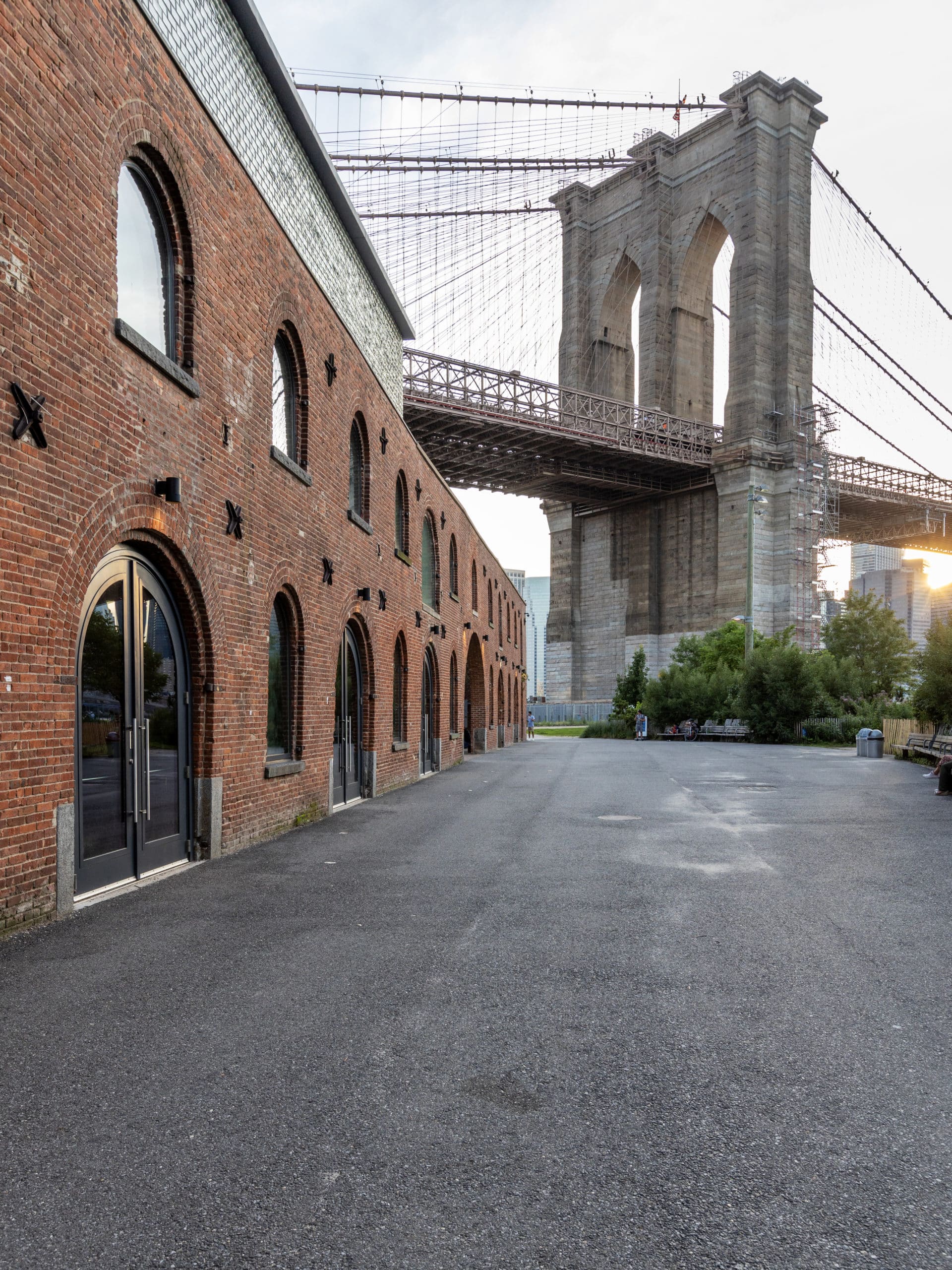 Exterior of St Ann's Warehouse at sunset with the Brooklyn Bridge overhead.