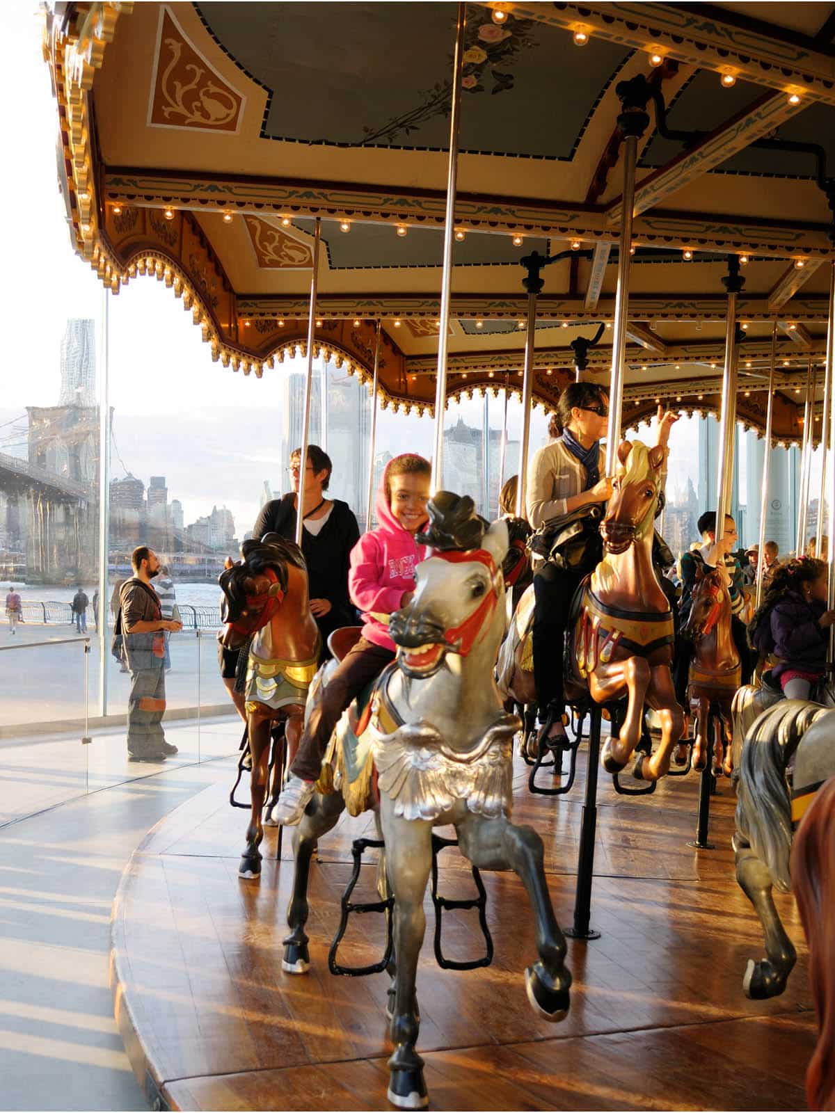 Children and adults on horses on Jane's Carousel at sunset.
