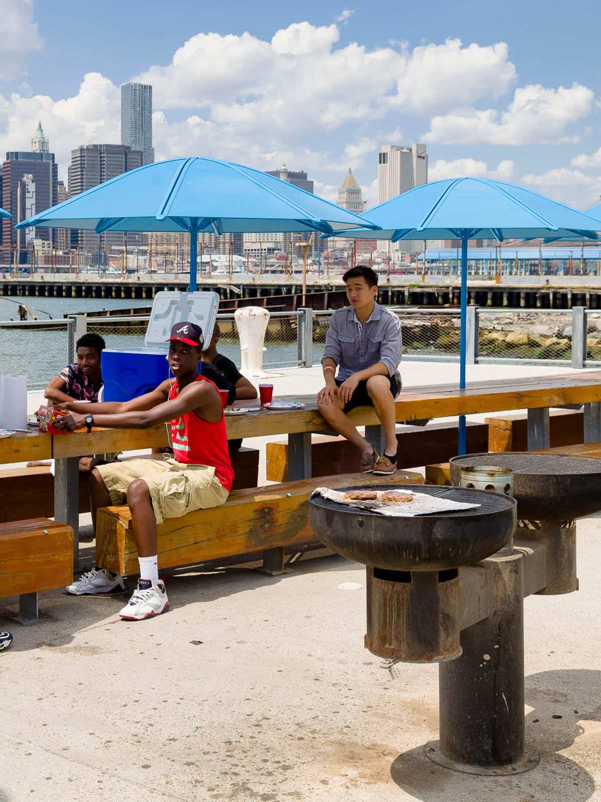 Men sitting at a picnic table with burgers on a grill on a sunny day.