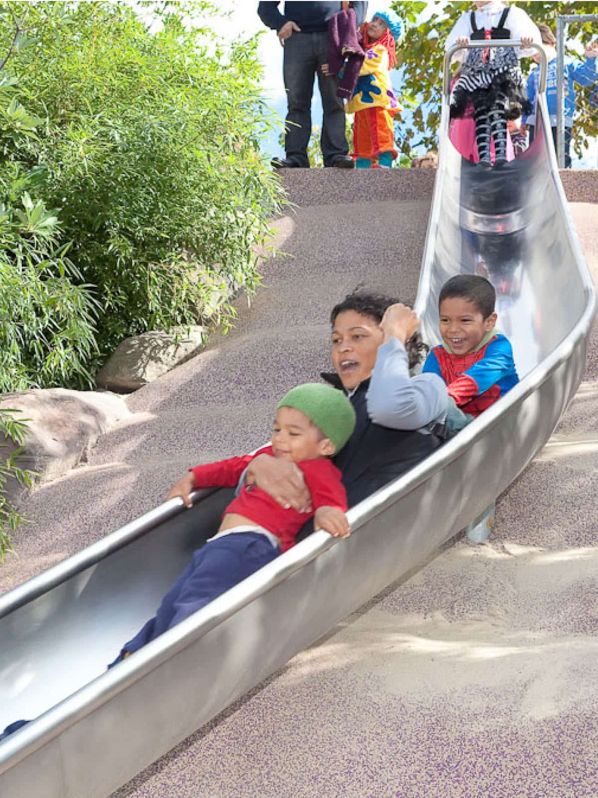 Mother and two children sliding down a slide on a sunny day.