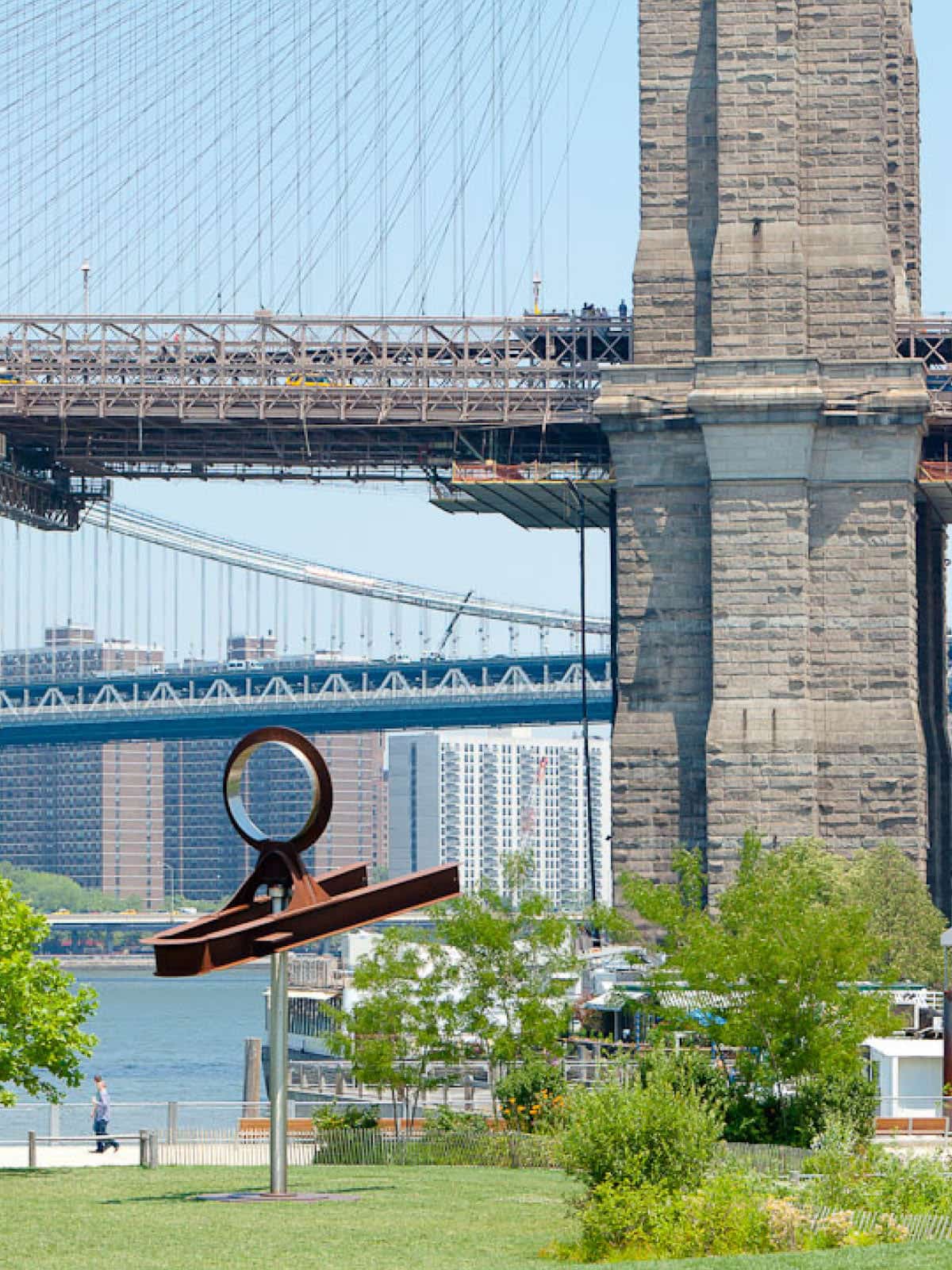 Yoga by Mark di Suvero on Pier 1 Lawn on a sunny day. The Brooklyn Bridge is seen in the background.