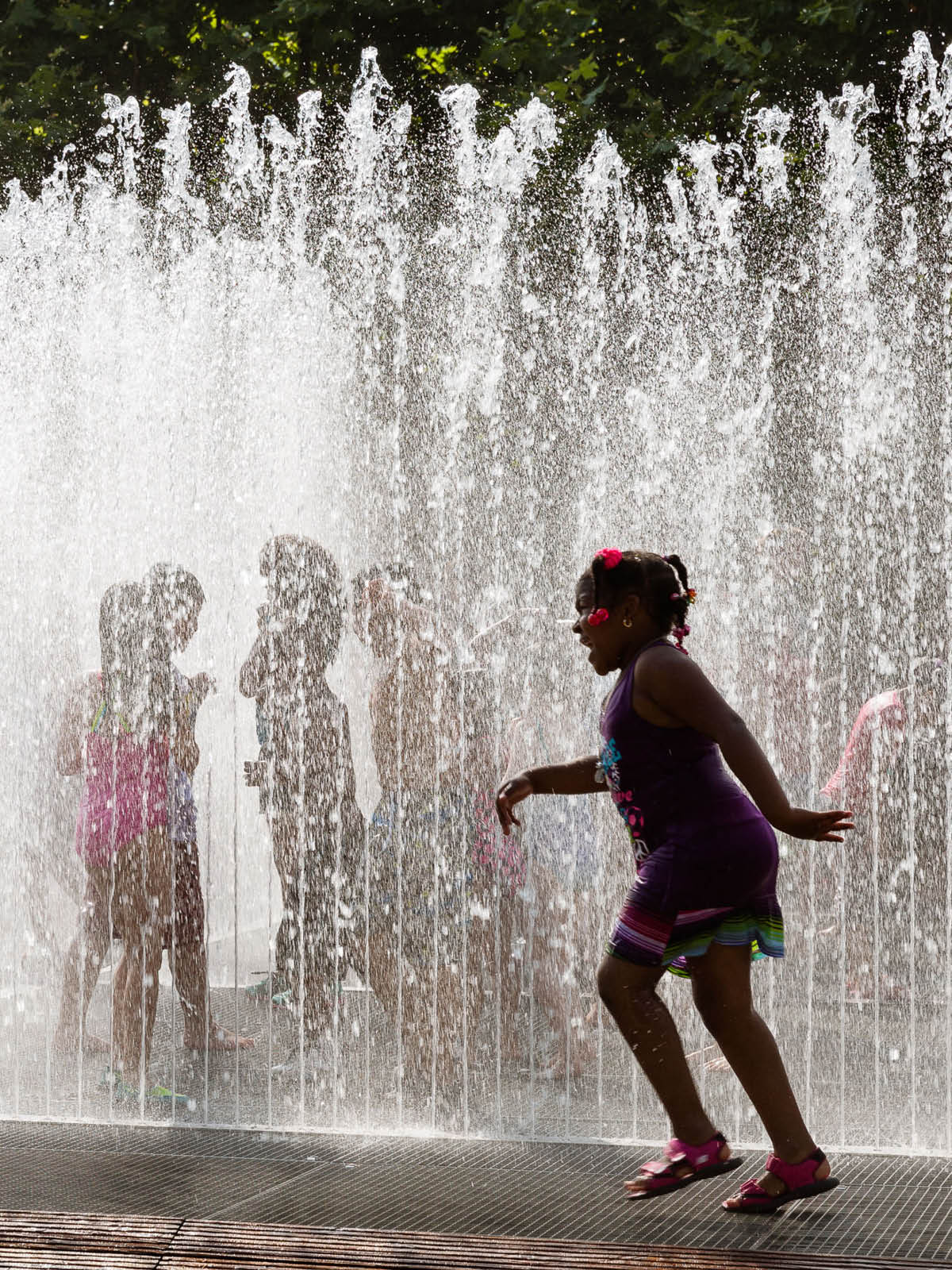 Children running through jets of water on a sunny day.
