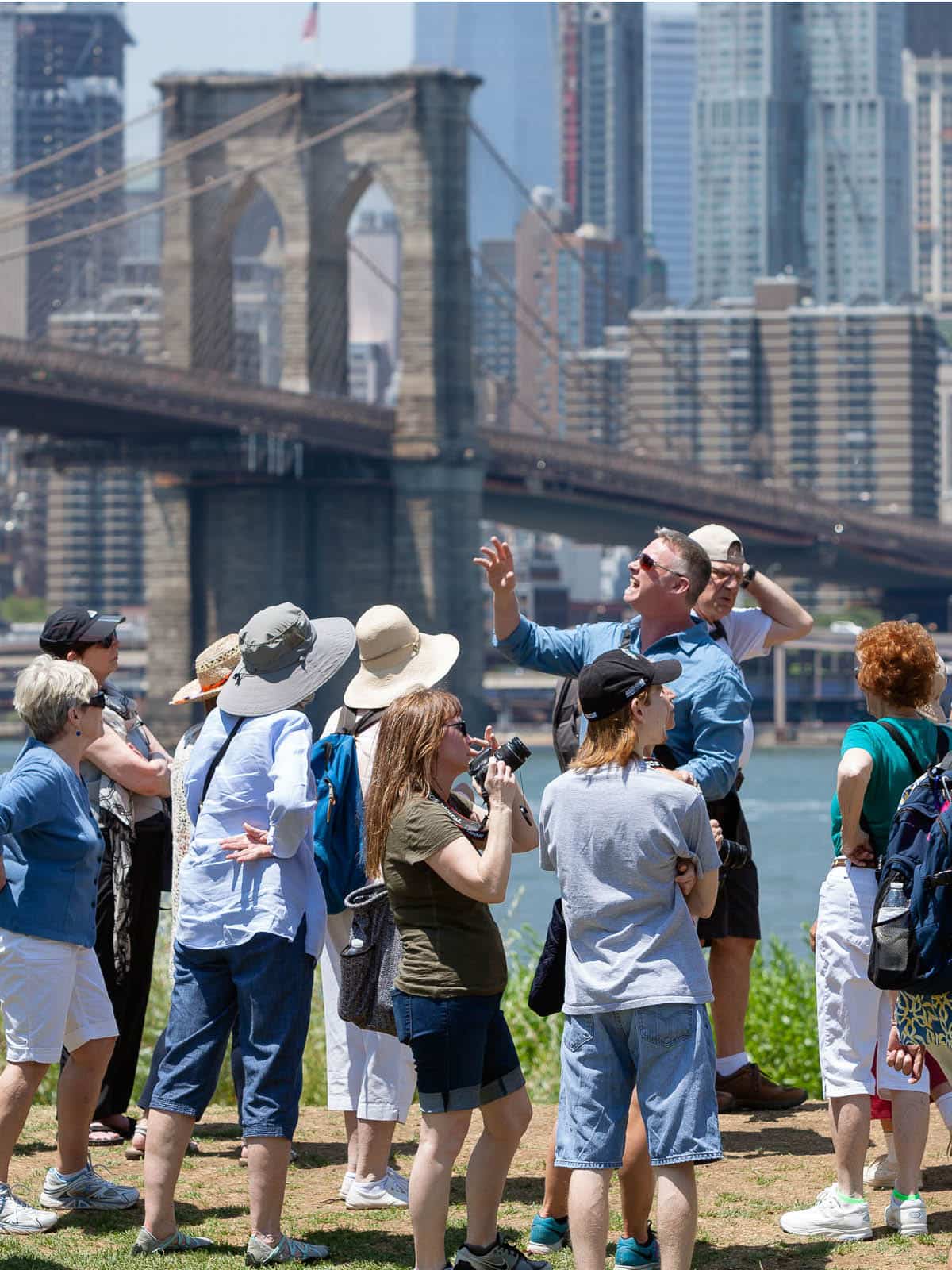 Tour guide points up in front of group with the Brooklyn Bridge in the background.